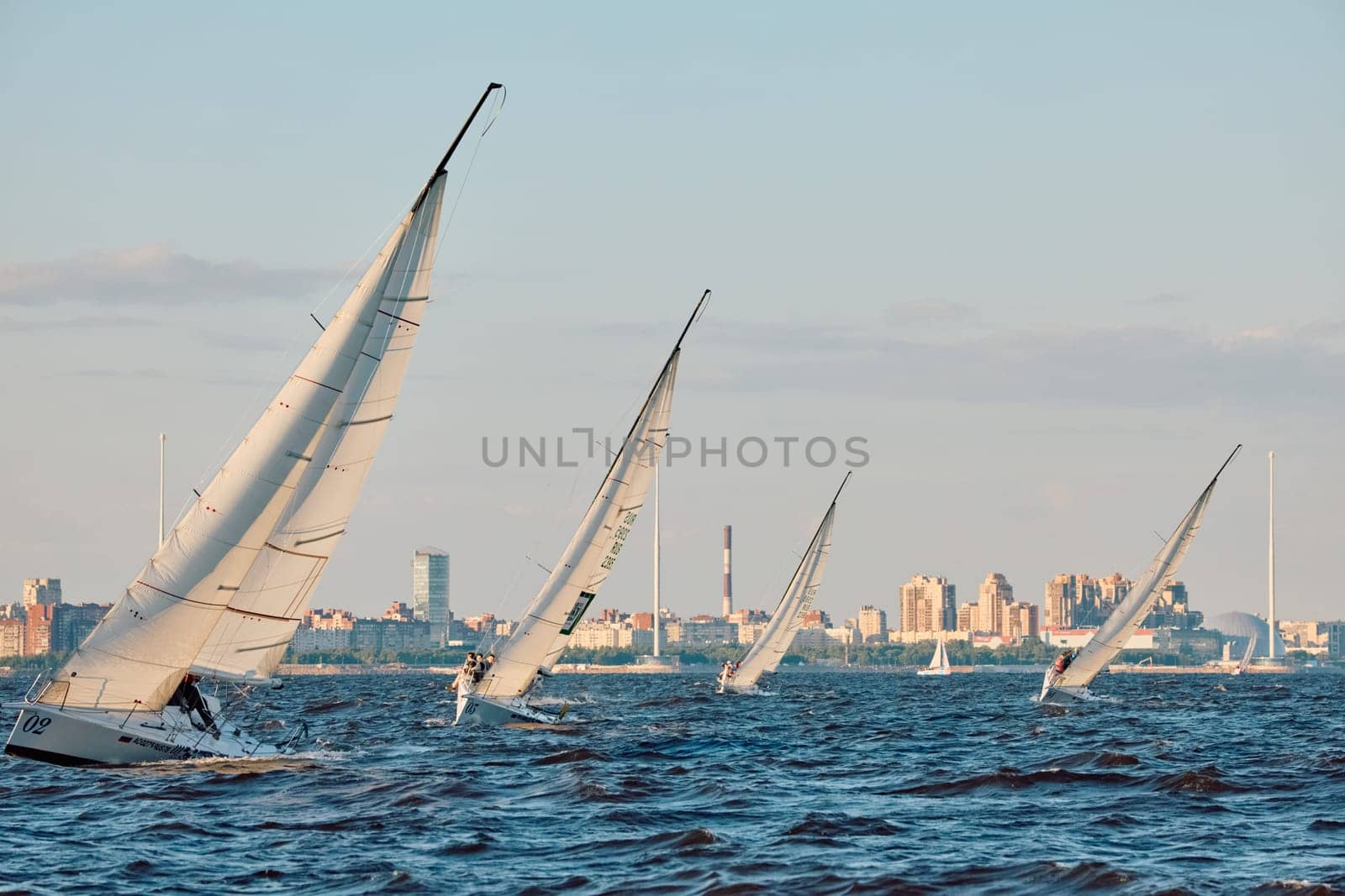 Russia, St.Petersburg, 07 June 2024: Sailing regatta in the Gulf of Finland at sunset, hot race of several yachts, teamwork, yachtsmen sitting on board the boat. High quality photo