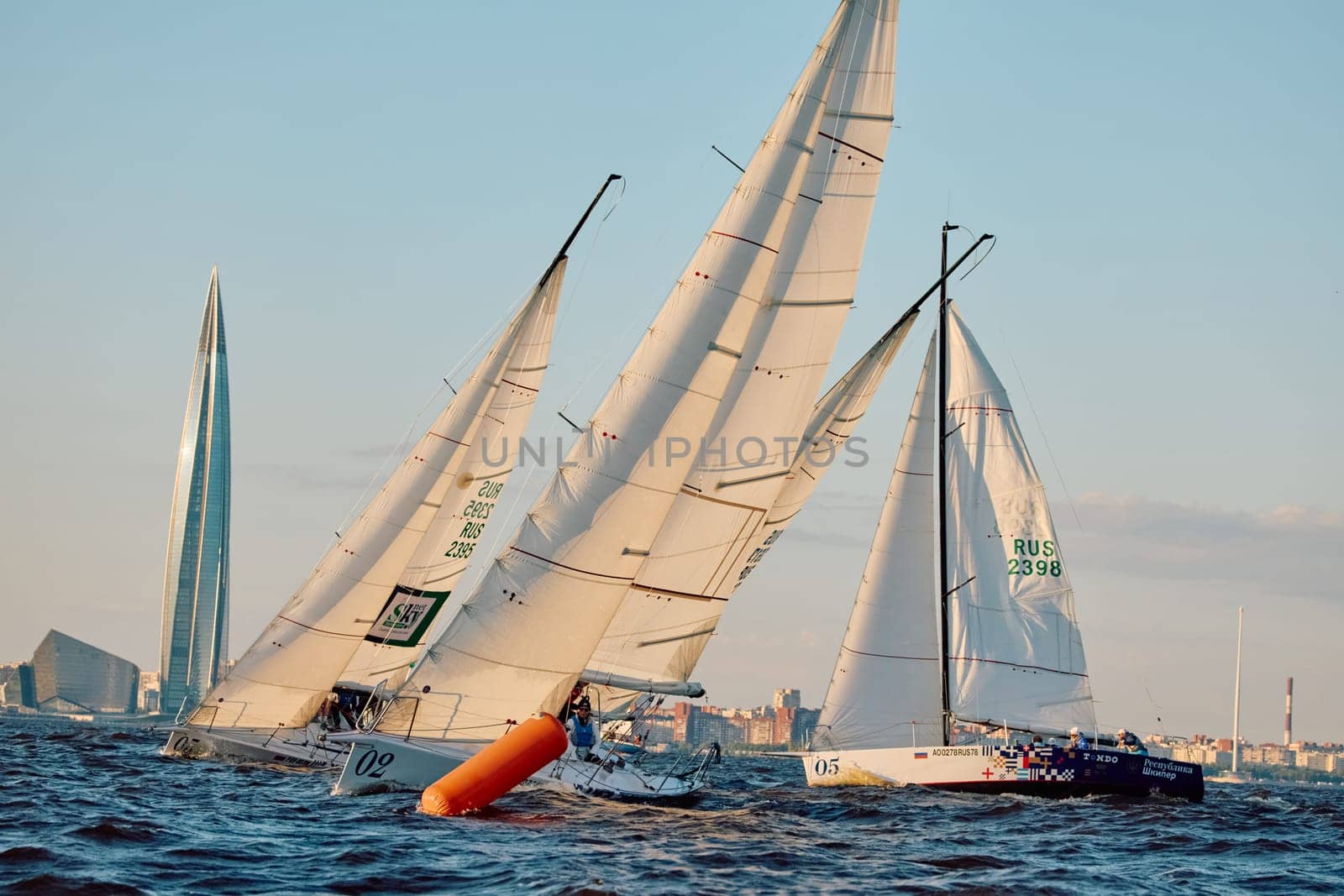Russia, St.Petersburg, 07 June 2024: Sailing regatta in the Gulf of Finland at sunset, hot race of several yachts, teamwork, yachtsmen sitting on board the boat. High quality photo