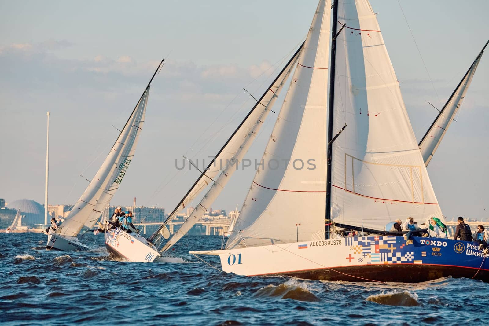 Russia, St.Petersburg, 07 June 2024: Sailing regatta in the Gulf of Finland at sunset, hot race of several yachts, teamwork, yachtsmen sitting on board the boat. High quality photo