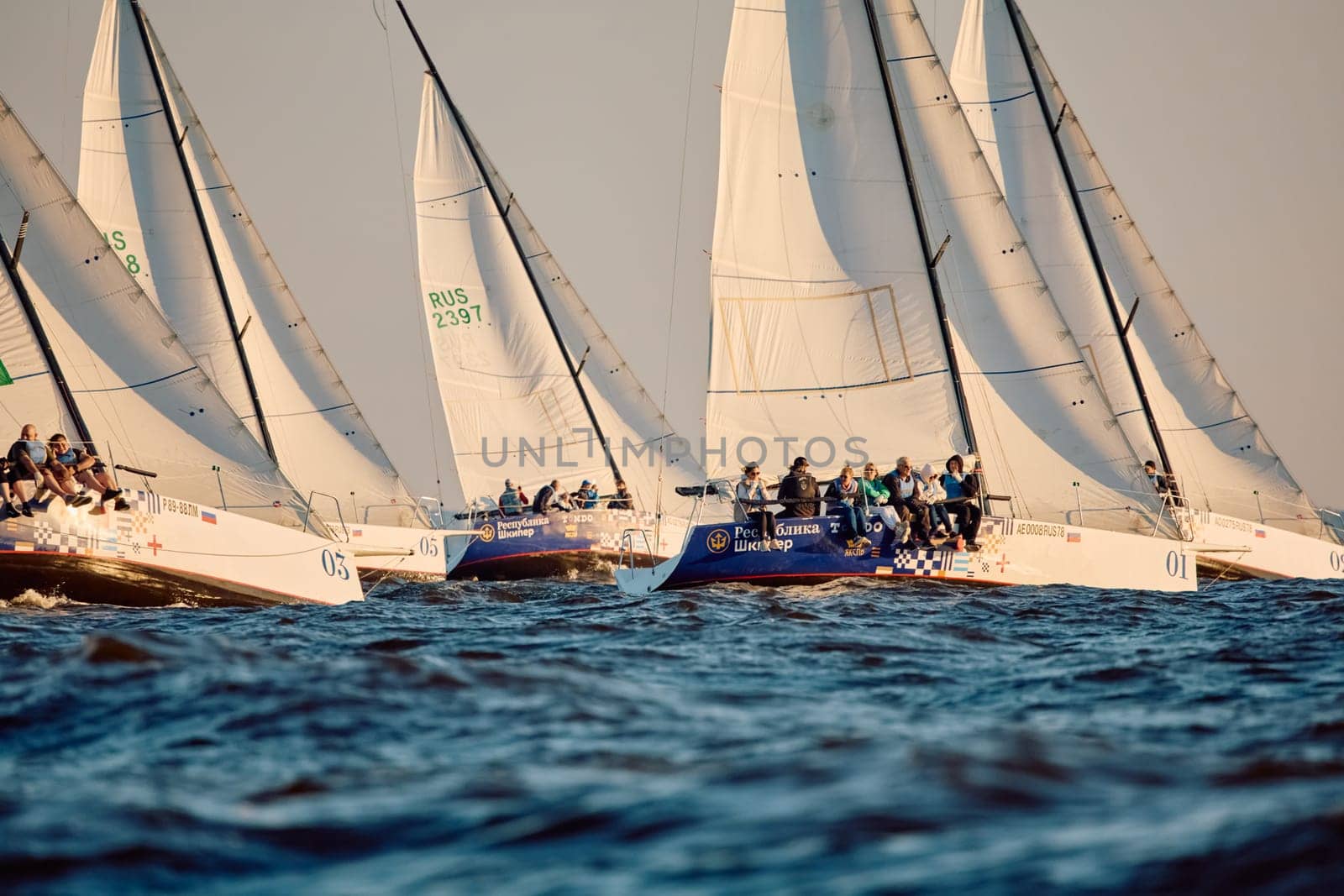 Russia, St.Petersburg, 07 June 2024: Sailing regatta in the Gulf of Finland at sunset, hot race of several yachts, teamwork, yachtsmen sitting on board the boat. High quality photo