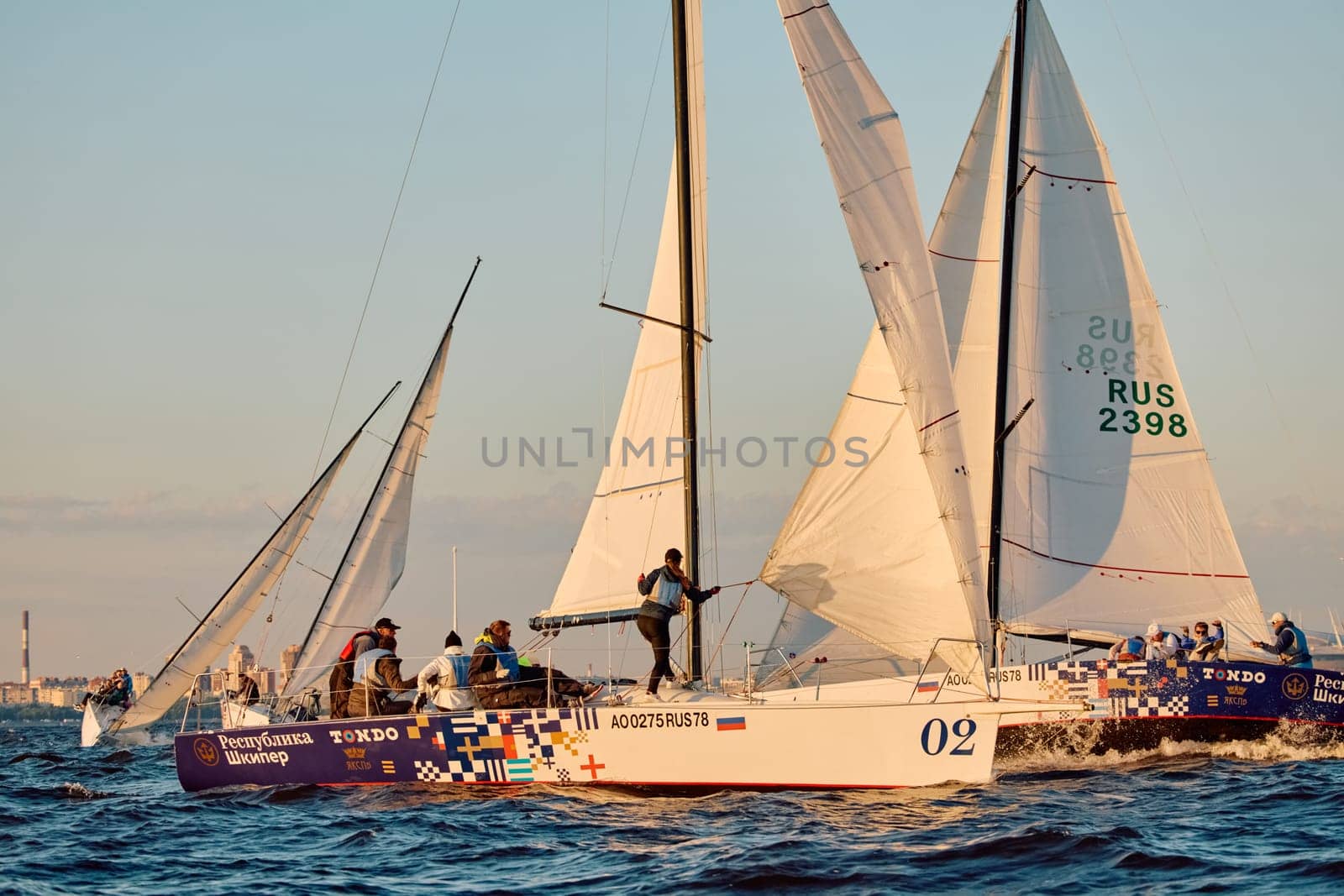 Russia, St.Petersburg, 07 June 2024: Sailing regatta in the Gulf of Finland at sunset, hot race of several yachts, teamwork, yachtsmen sitting on board the boat. High quality photo