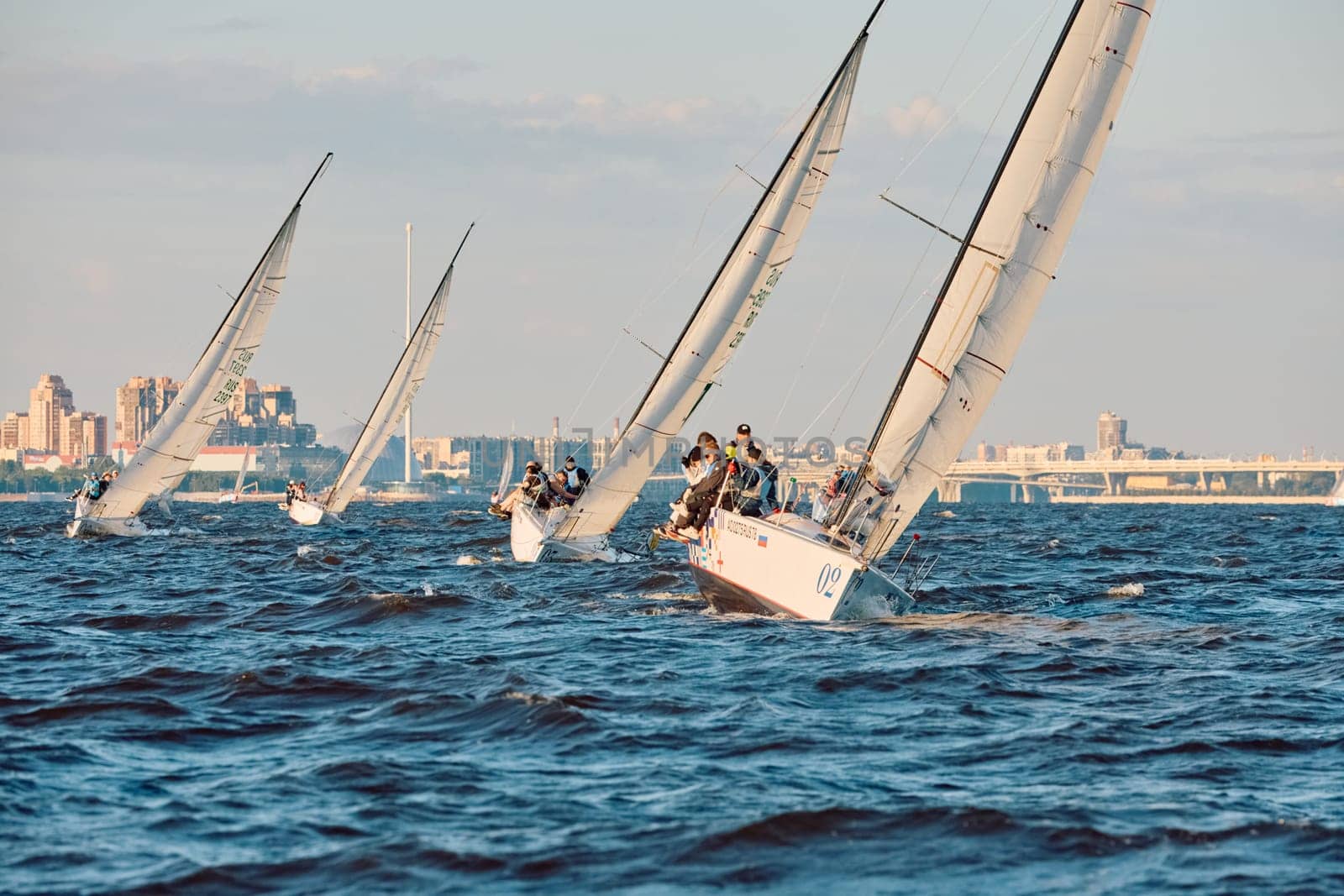 Russia, St.Petersburg, 07 June 2024: Sailing regatta in the Gulf of Finland at sunset, hot race of several yachts, teamwork, yachtsmen sitting on board the boat. High quality photo