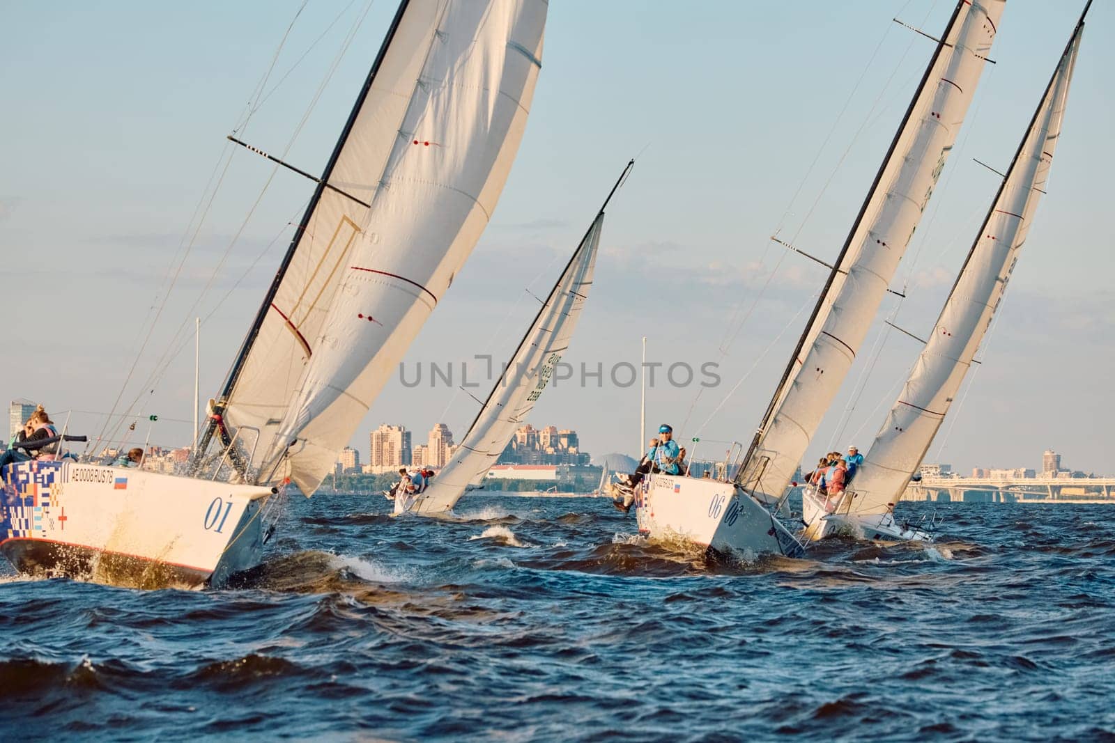 Russia, St.Petersburg, 07 June 2024: Sailing regatta in the Gulf of Finland at sunset, hot race of several yachts, teamwork, yachtsmen sitting on board the boat. High quality photo