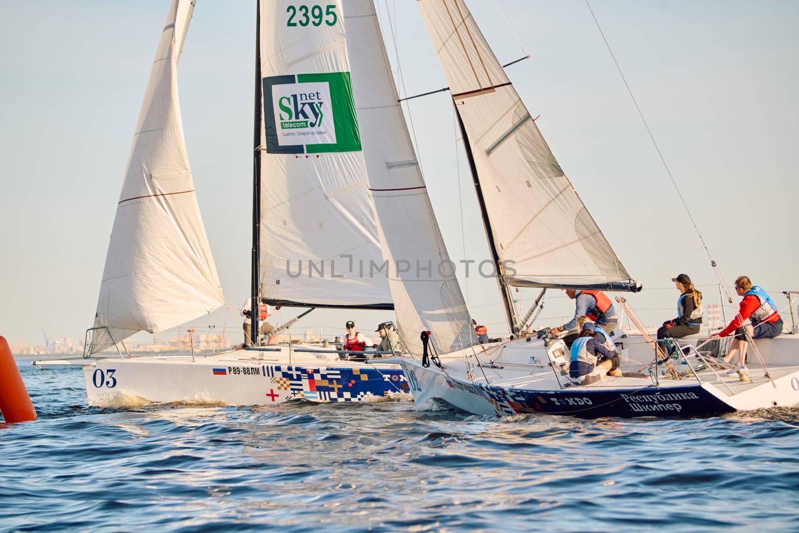 Russia, St.Petersburg, 24 May 2024: Sailing regatta in the Gulf of Finland at sunset, hot race of several yachts, teamwork, yachtsmen sitting on board the boat. High quality photo