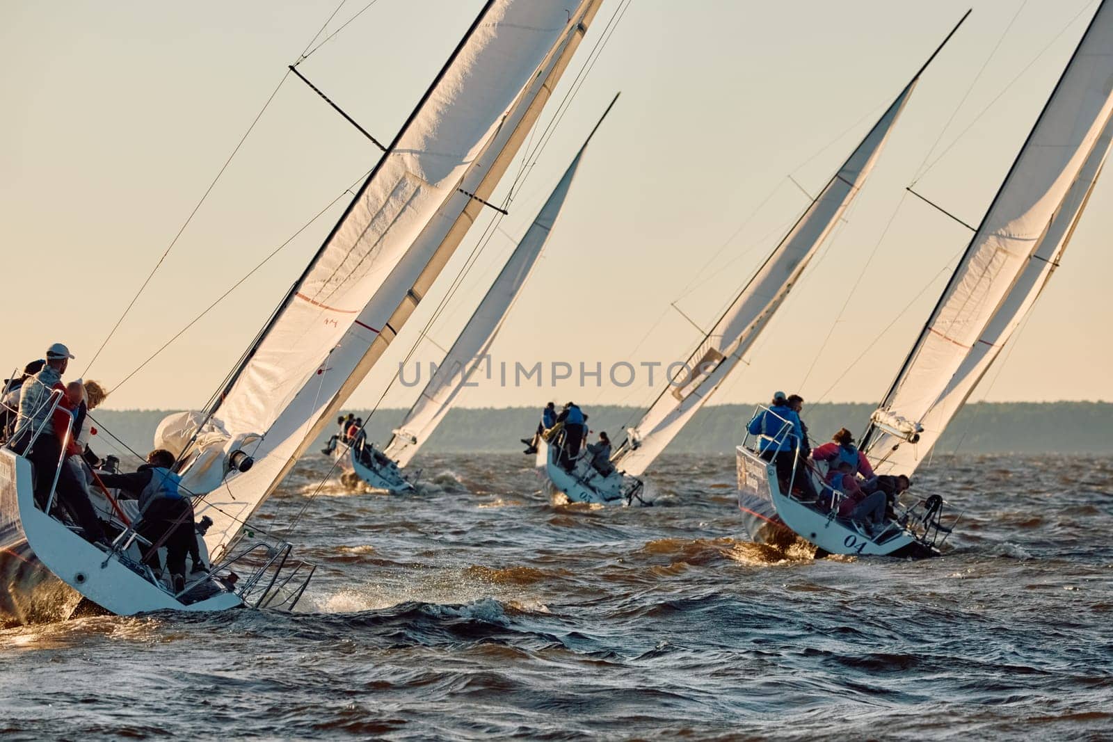 Russia, St.Petersburg, 07 June 2024: Sailing regatta in the Gulf of Finland at sunset, hot race of several yachts, teamwork, yachtsmen sitting on board the boat. High quality photo