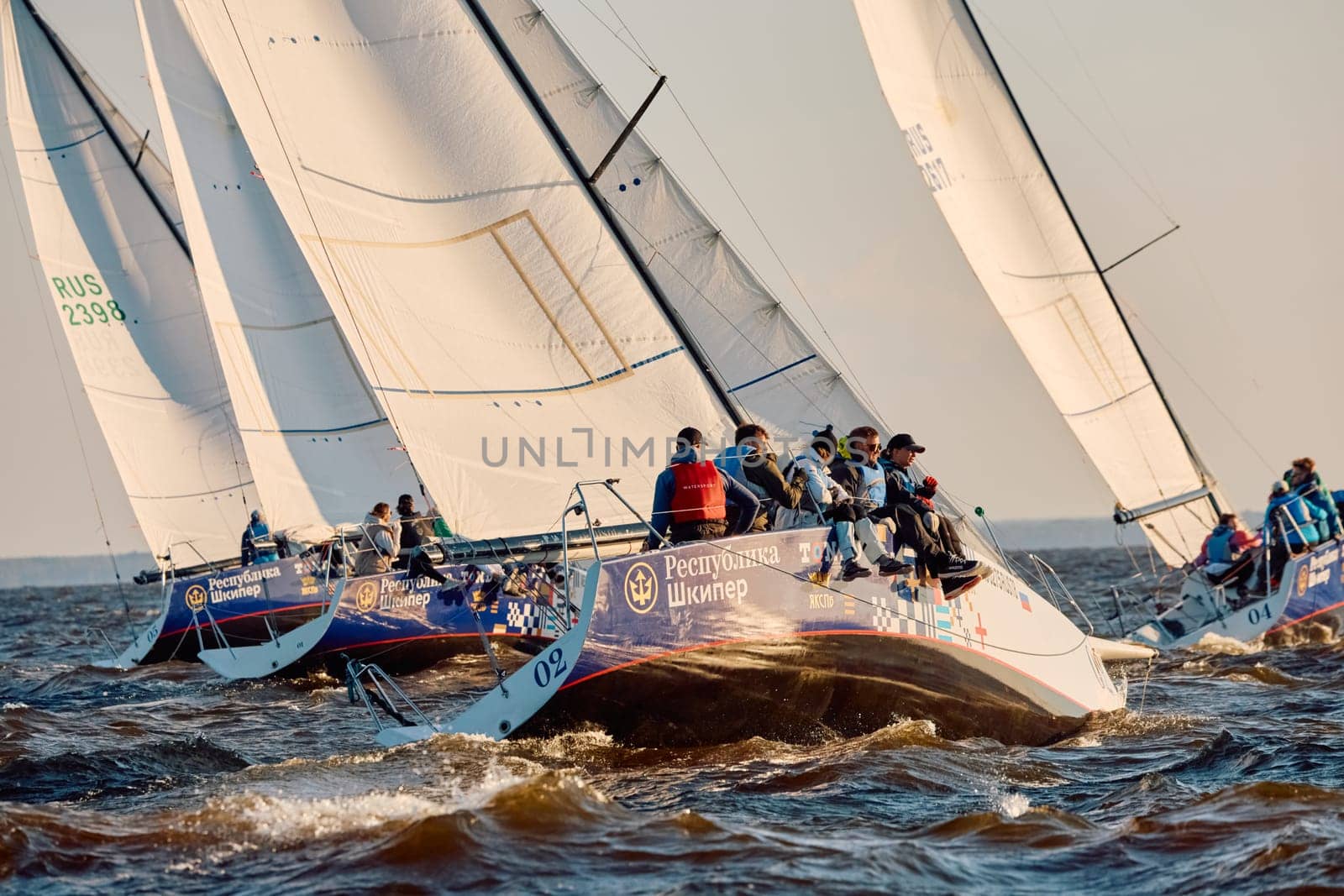Russia, St.Petersburg, 07 June 2024: Sailing regatta in the Gulf of Finland at sunset, hot race of several yachts, teamwork, yachtsmen sitting on board the boat. High quality photo