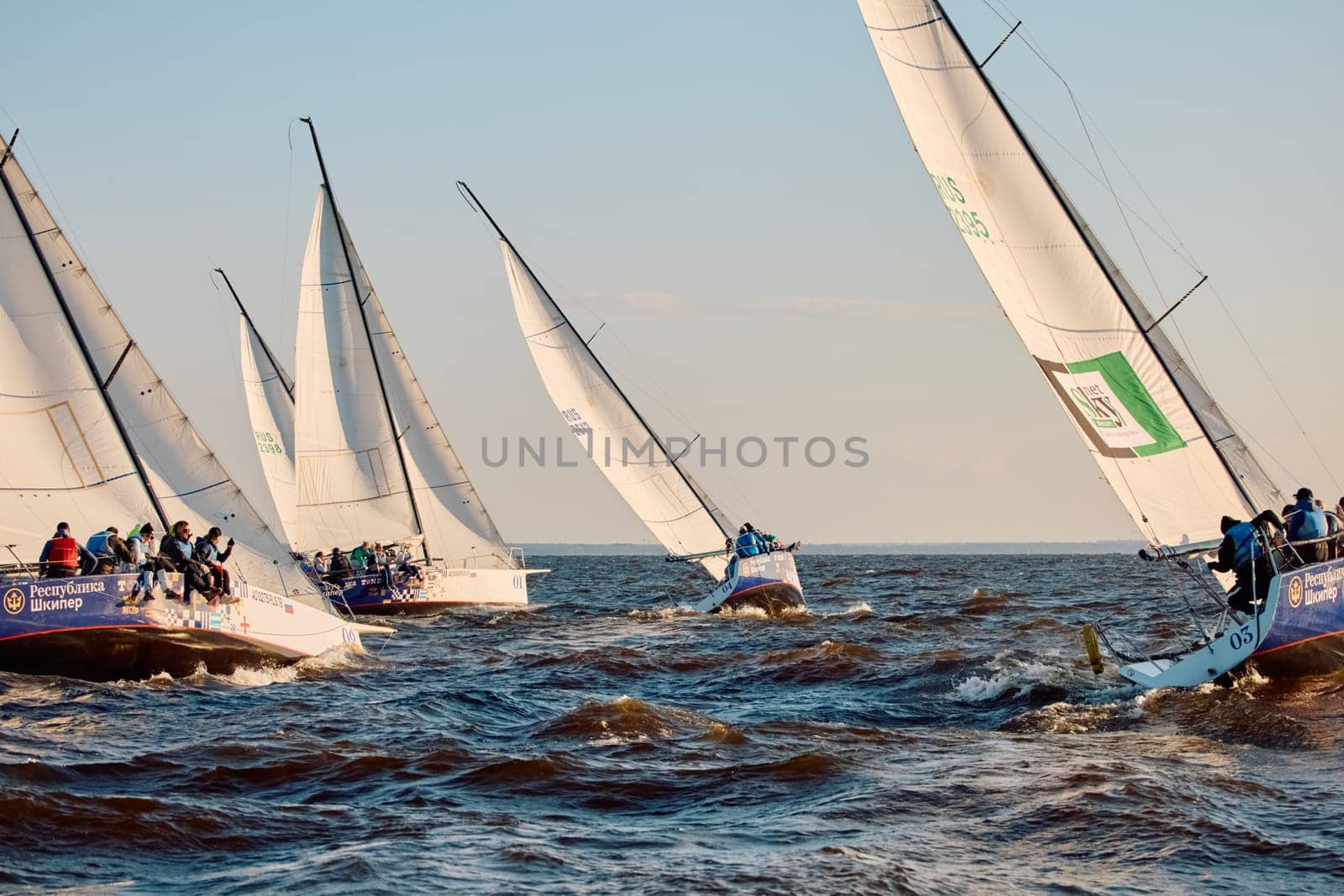 Russia, St.Petersburg, 07 June 2024: Sailing regatta in the Gulf of Finland at sunset, hot race of several yachts, teamwork, yachtsmen sitting on board the boat. High quality photo