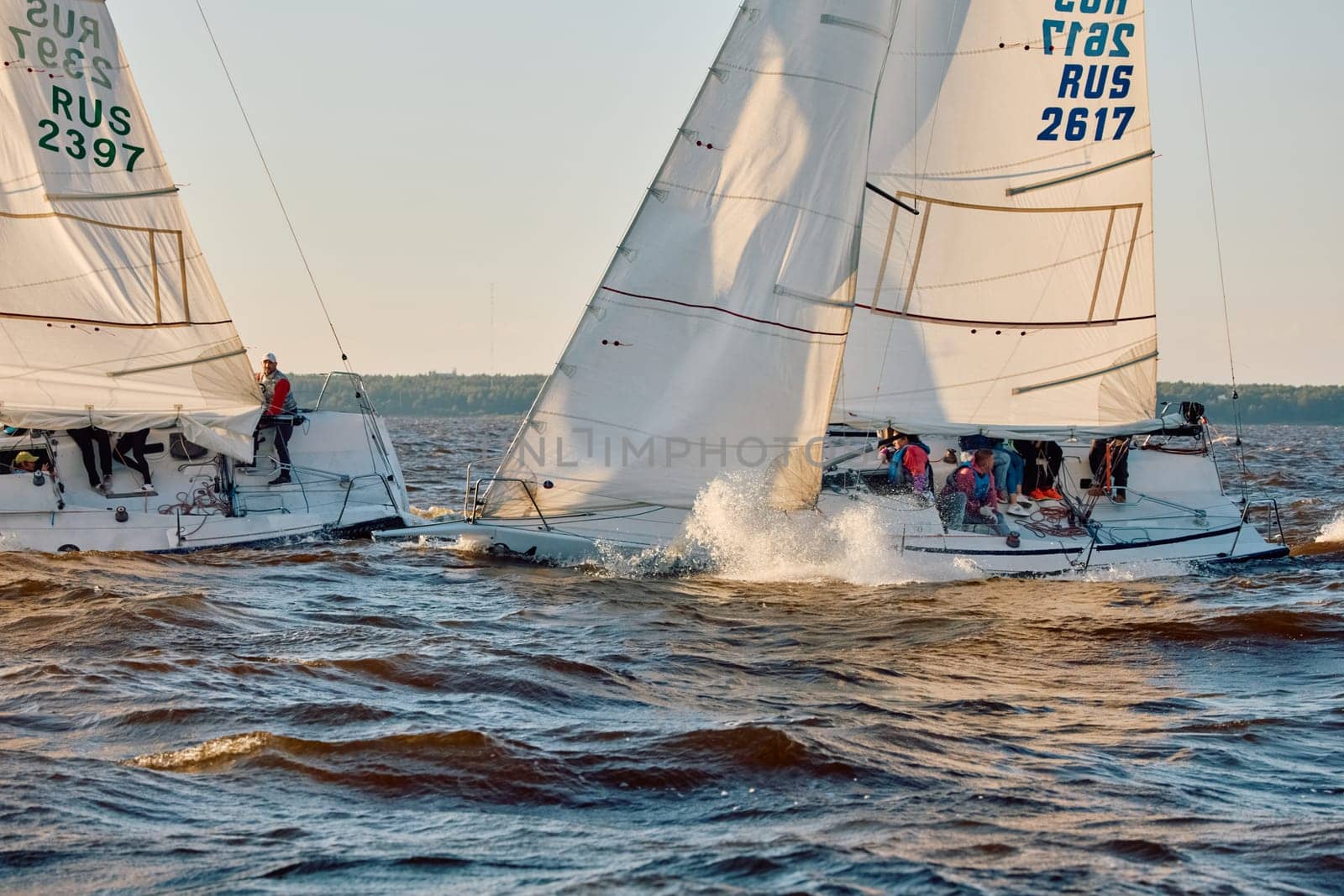 Russia, St.Petersburg, 07 June 2024: Sailing regatta in the Gulf of Finland at sunset, hot race of several yachts, teamwork, yachtsmen sitting on board the boat. High quality photo