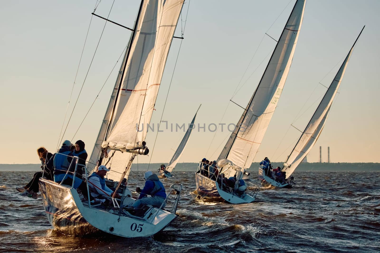 Russia, St.Petersburg, 07 June 2024: Sailing regatta in the Gulf of Finland at sunset, hot race of several yachts, teamwork, yachtsmen sitting on board the boat. High quality photo