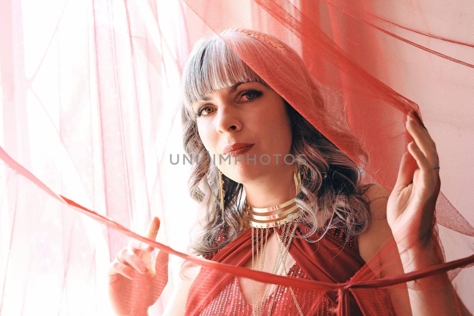 A pretty woman in a red dress looks through a curtain