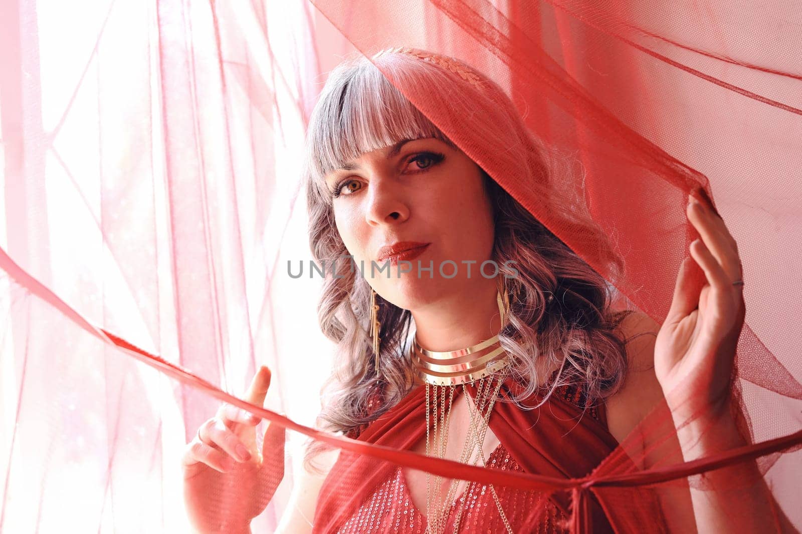 A pretty woman in a red dress looks through a curtain