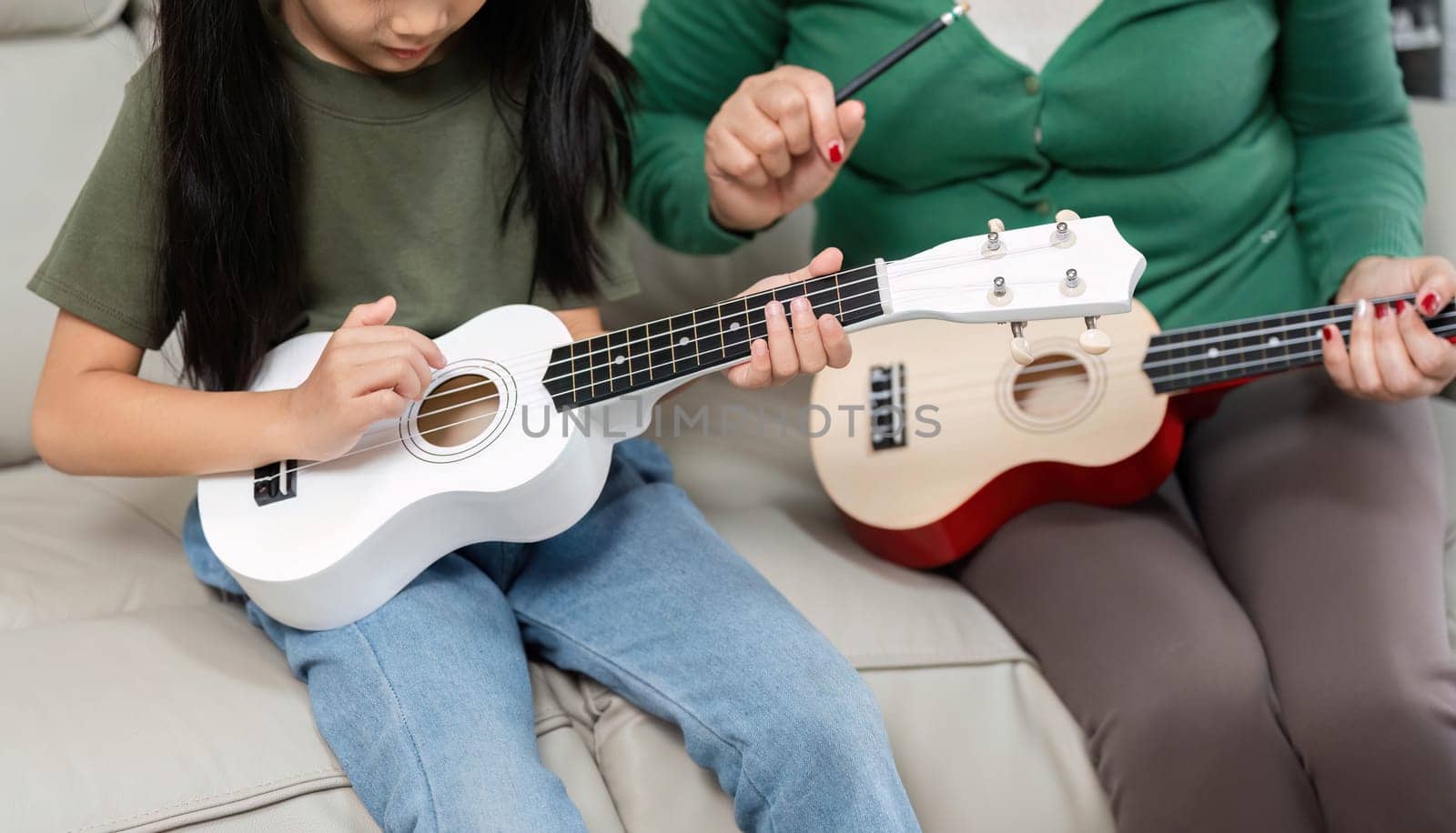 A mother patiently guides her daughter in learning the ukulele, emphasizing the importance of music education and family bonding.
