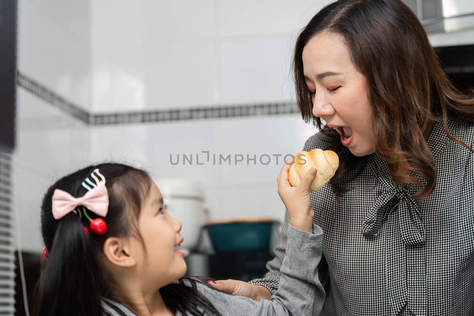 A little girl playfully offers a pastry to her mother, creating a joyful and engaging moment in the kitchen.