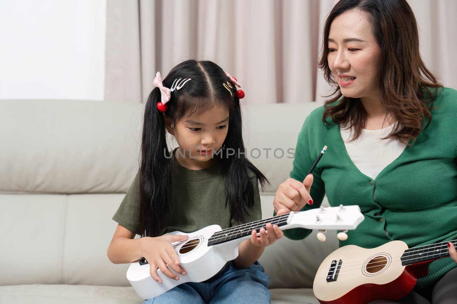 A joyful moment of a mother guiding her daughter in playing the ukulele, fostering a love for music and creativity in a cozy home setting.