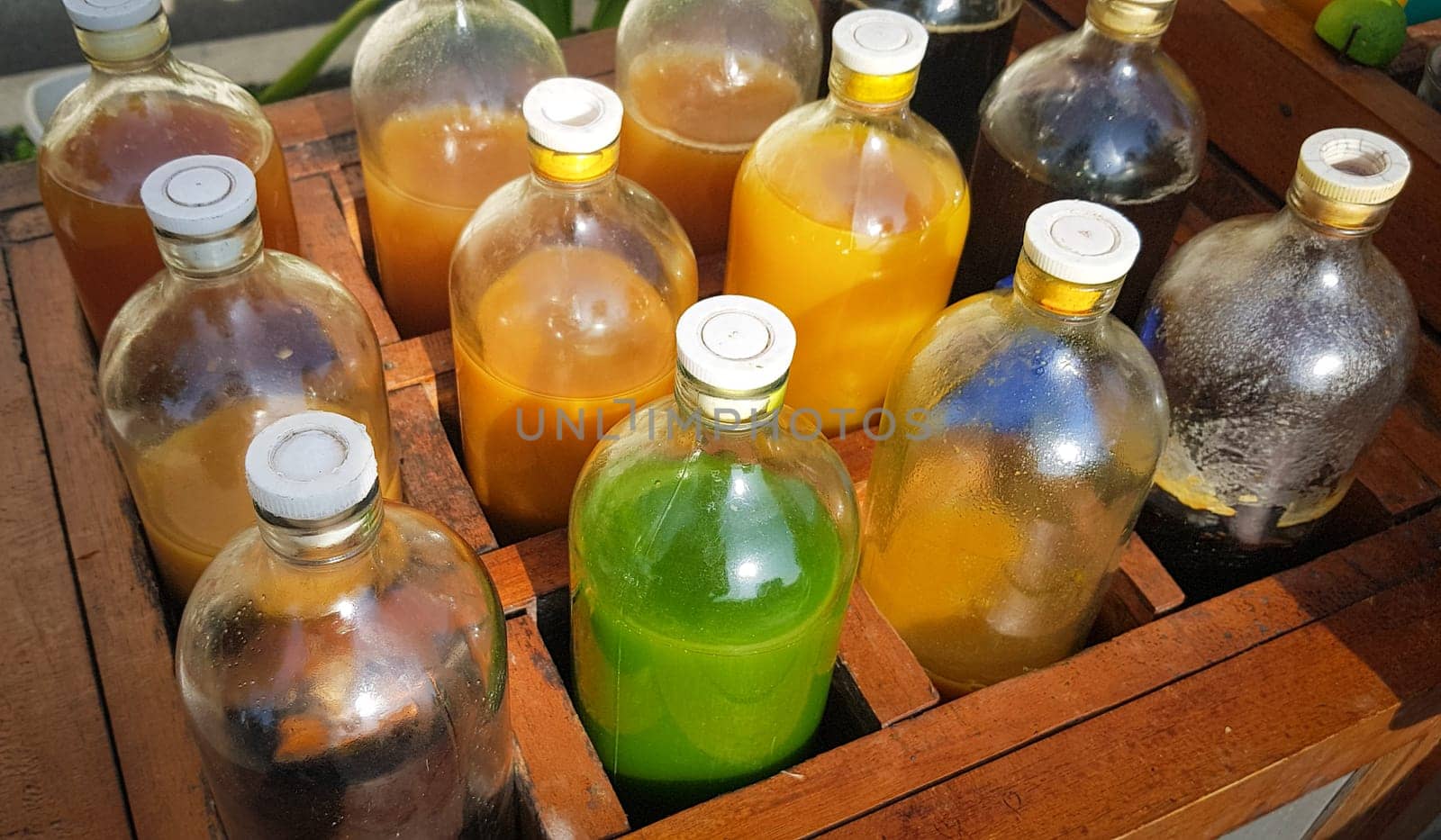Colorful Bottles of traditional natural organic medicine locally called jamu, Displayed in Wooden Case on a Sunny Day, Various colorful bottles filled with liquids arranged in a wooden container outdoors under sunlight.
