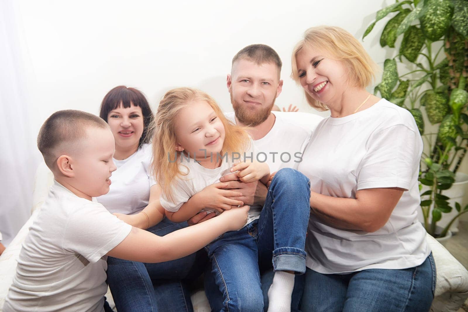 A joyful family engages in playful activities indoors, wearing matching casual outfits and sharing laughter together on a cozy couch.