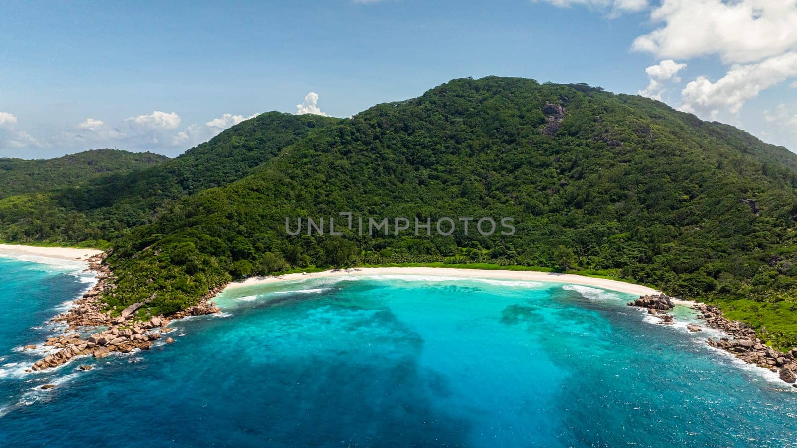 Aerial view of a tropical coastline with lush green hills and clear ocean water. La Digue, Seychelles.