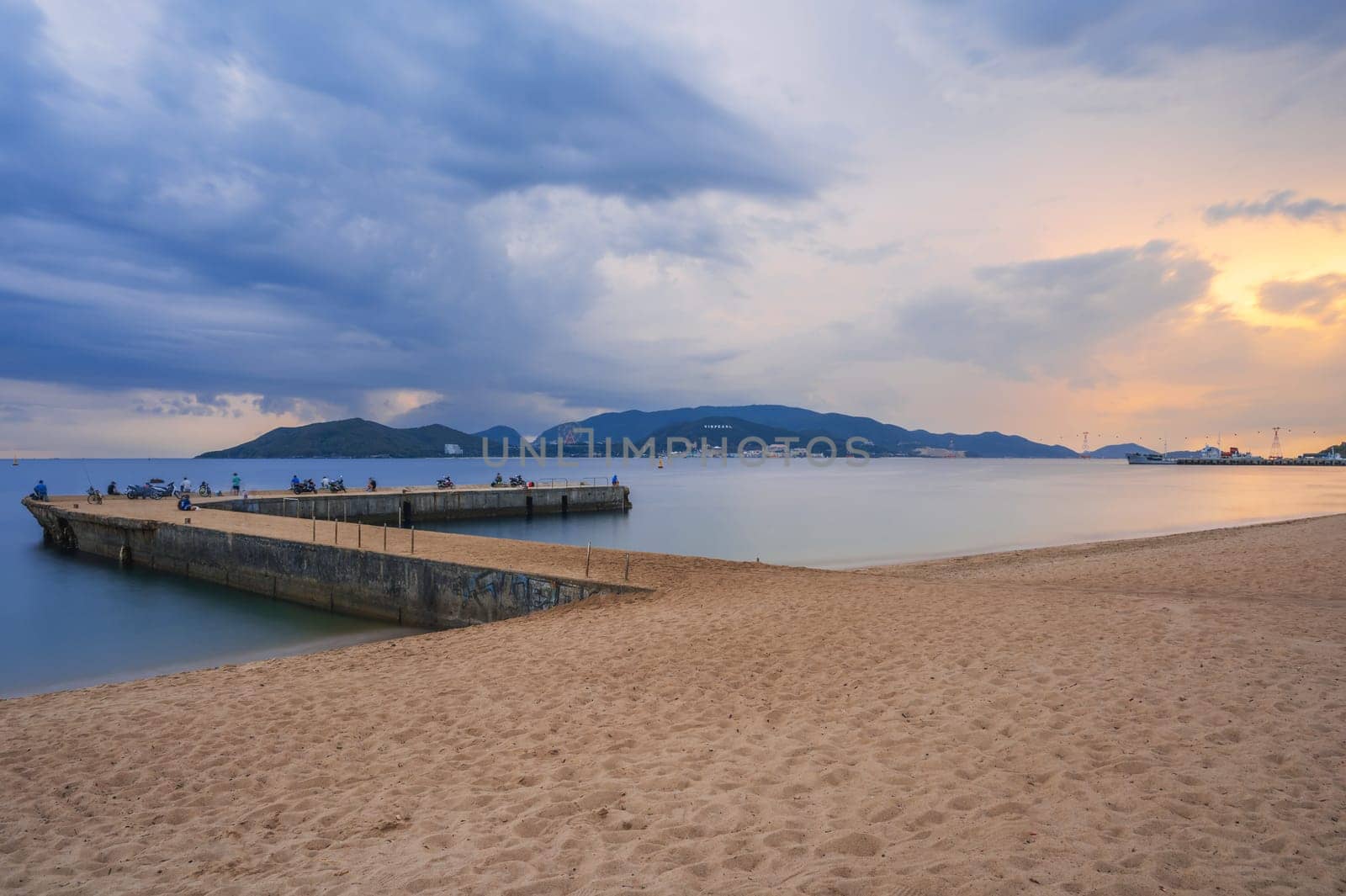 Pier with fishermen in sea at sandy beach at sunrise in the morning. View of Vinpearl Island in Nha Trang in Vietnam. Long exposure landscape