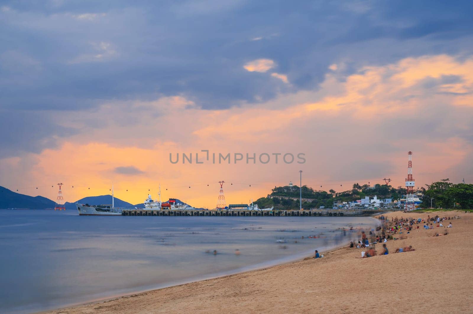 pier with ships in port and sandy beach with tourists by the sea in the morning at dawn in Nha Trang, Vietnam