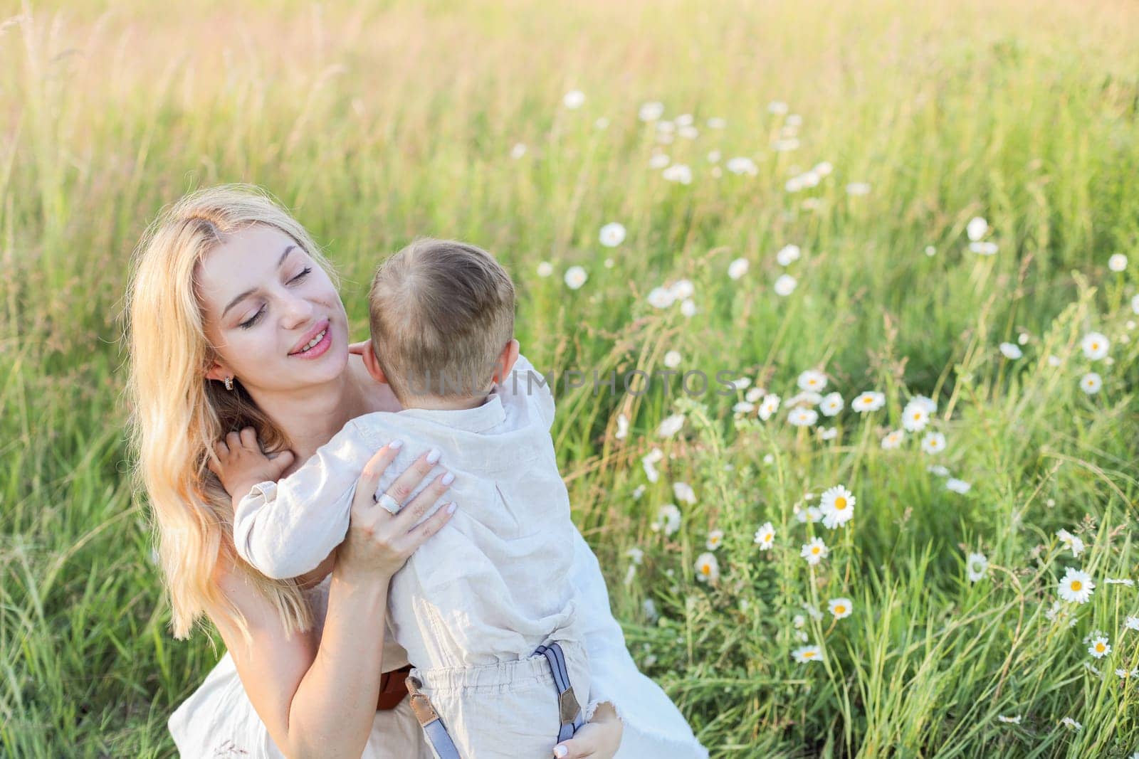Mom hugs little child in a meadow with daisies, cute mom and two-year-old child have fun in a summer field. High quality photo