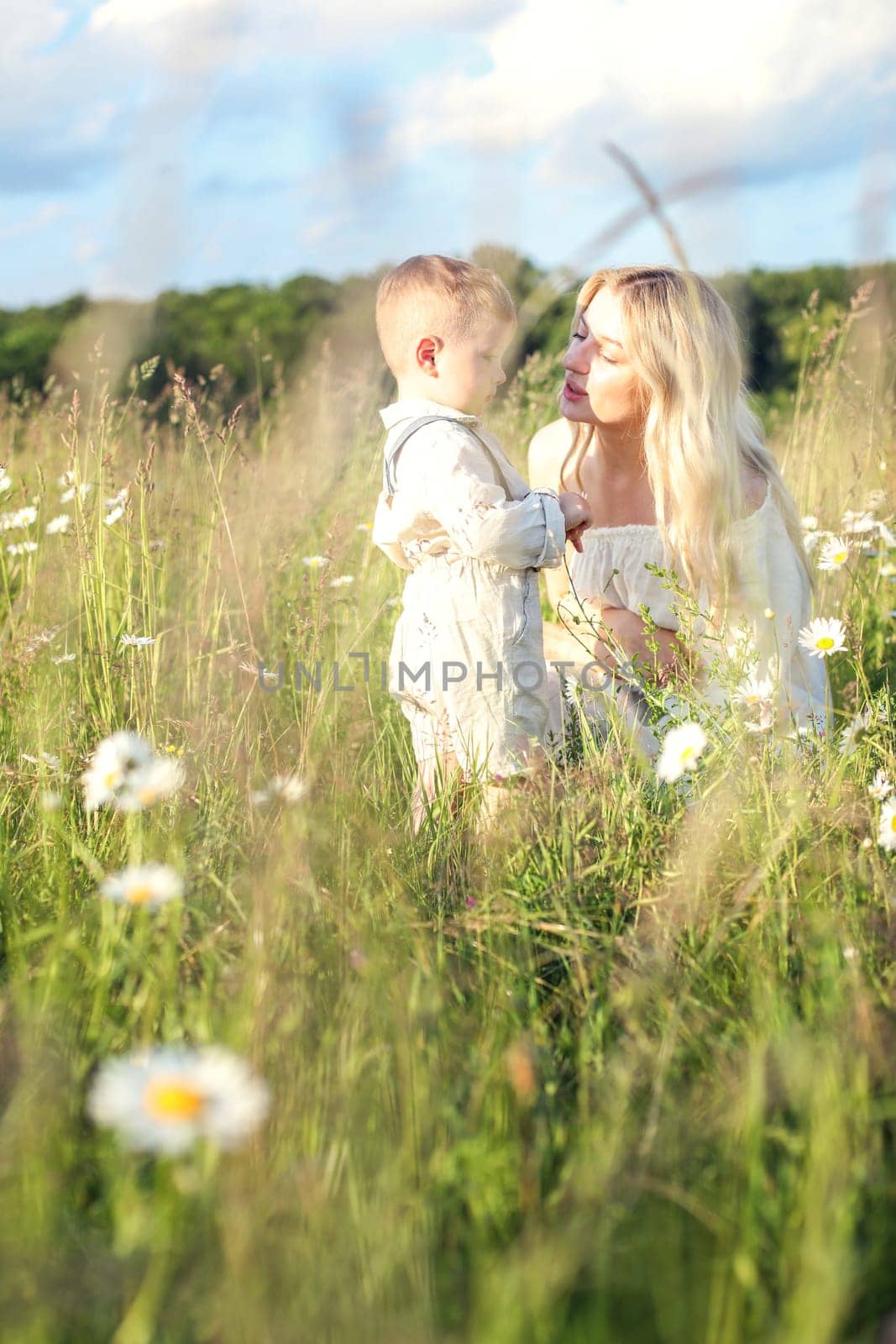 Mother and little child in a meadow with daisies resting and chatting. High quality photo
