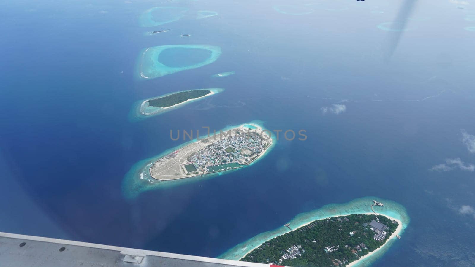 Airplane passenger enjoying the breathtaking view of the maldives islands, a tropical paradise with crystal-clear turquoise waters and lush green vegetation
