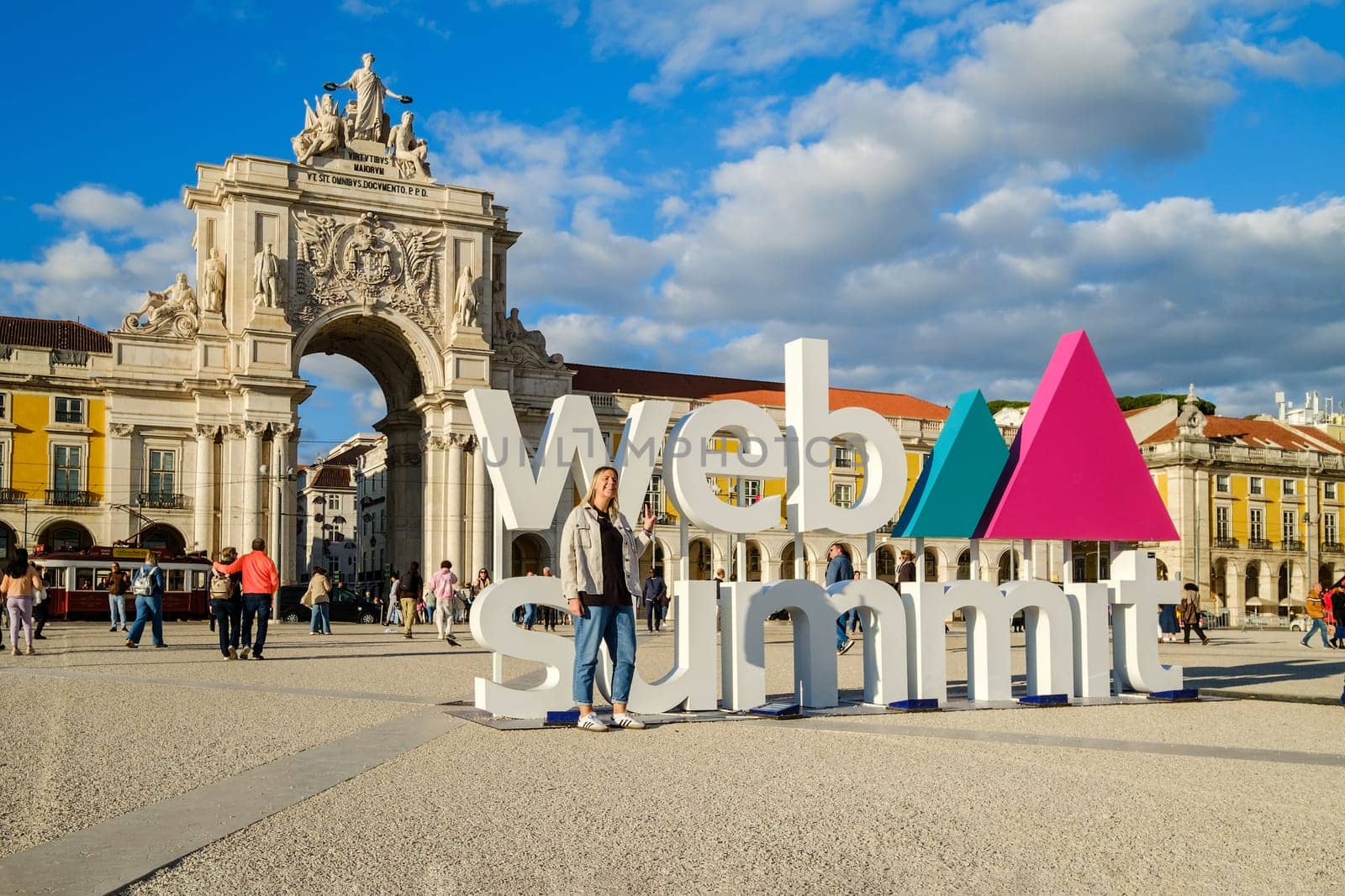 Nov 13, 2024 - Lisbon, Portugal: A female adult posing for a photo in front of Web Summit sign installation at Commerce square and Rua Augusta Arch. People walking, international technology conference, discussions, networking, technology, innovation