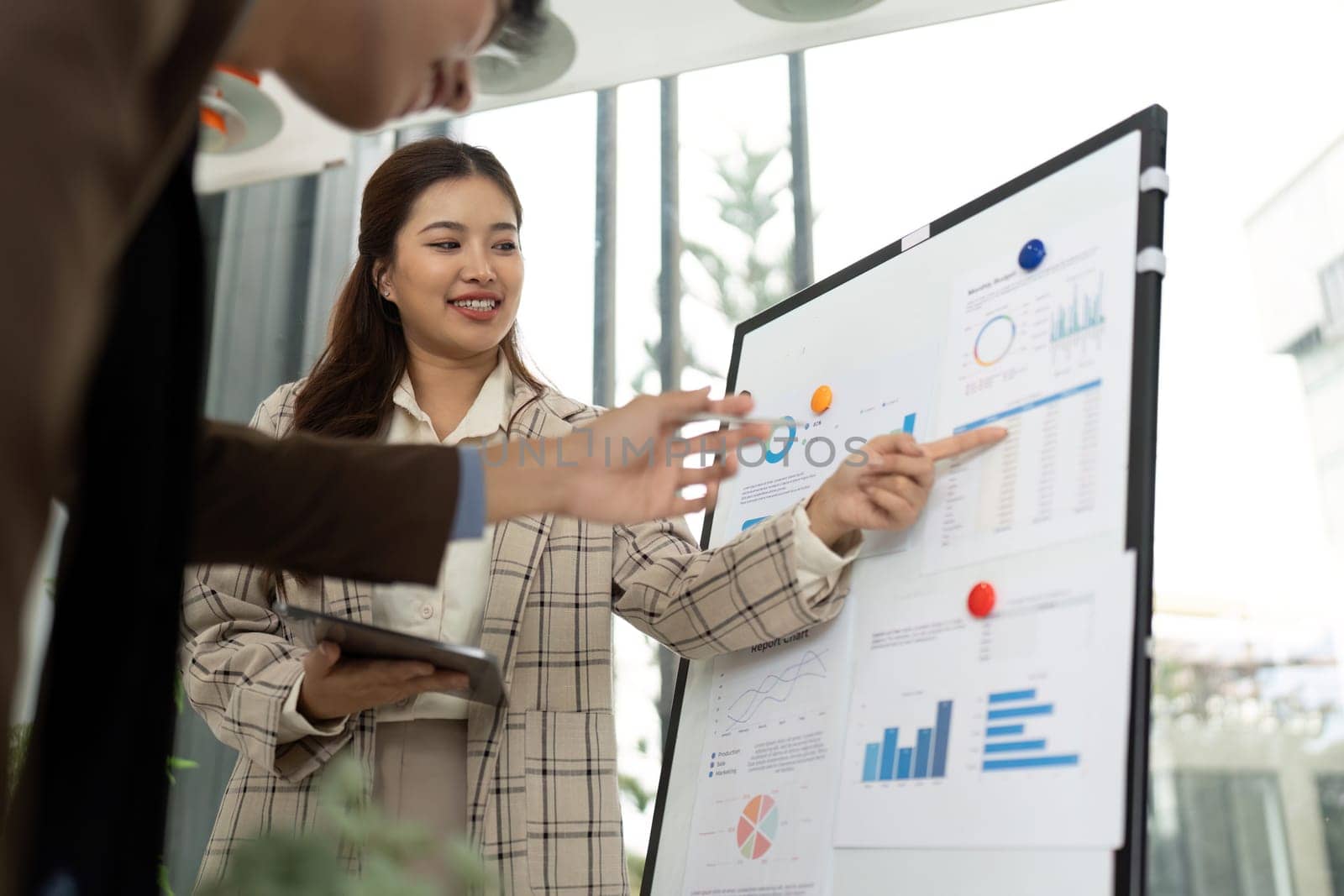 A businesswoman smiles as she points at data charts while discussing insights with a colleague in a contemporary office.