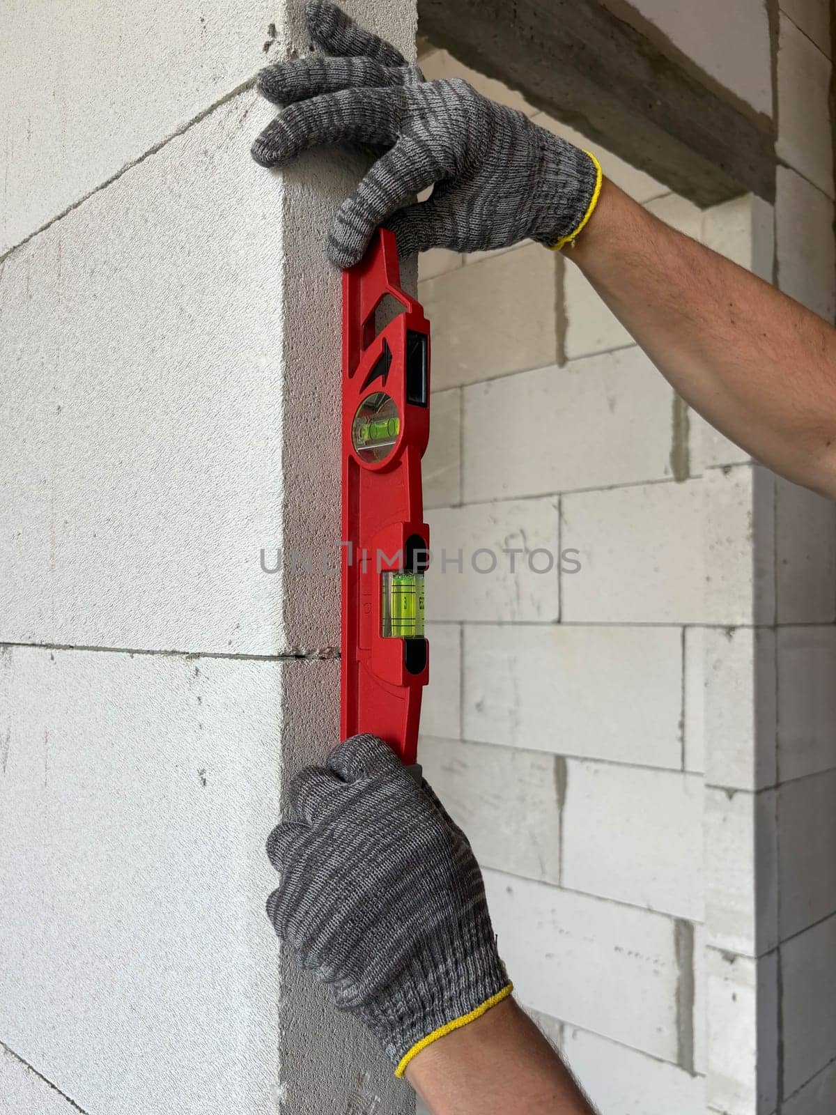 A close-up photo of a level in the hands of a builder measuring the evenness of a wall. A side view of the level on the wall. Construction and renovation of housing.