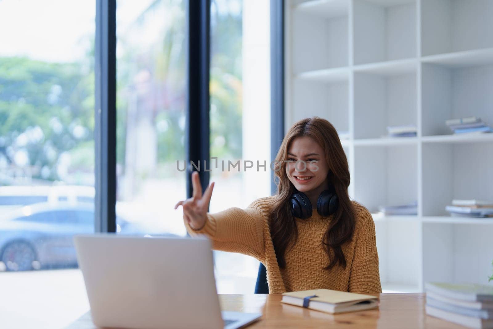 Smiling woman waves during a video conference on her laptop at her desk..