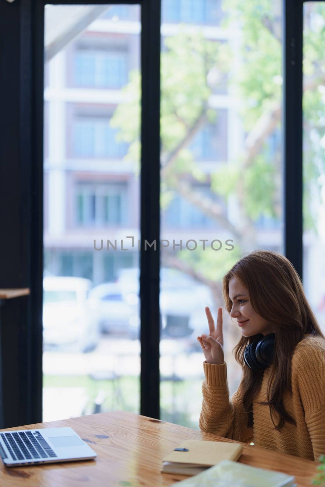 Young woman sits at a desk showing the peace sign near her laptop computer..