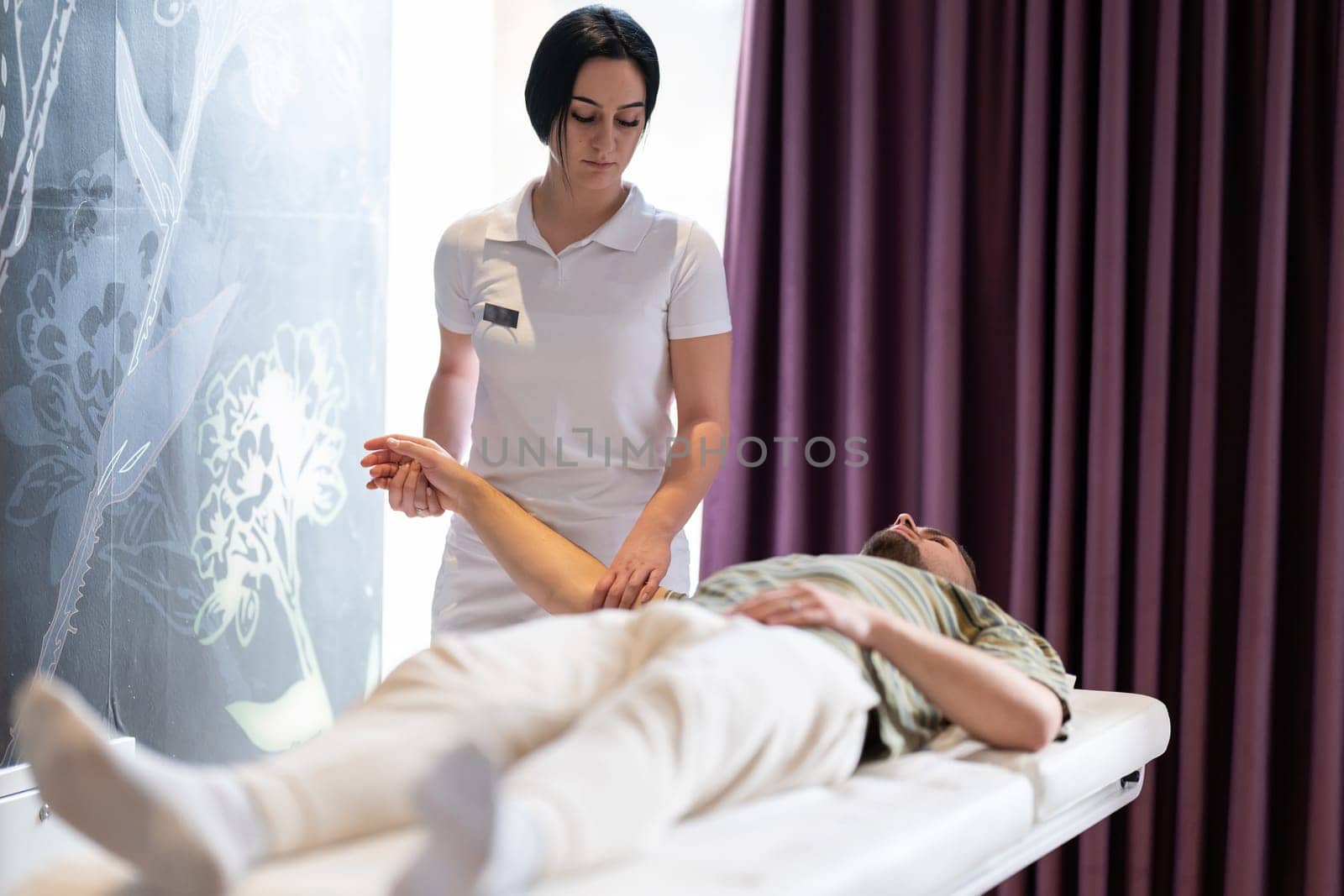 Therapist Performing Arm Stretch. A female therapist performs an arm stretch technique on a male patient lying on a treatment bed.