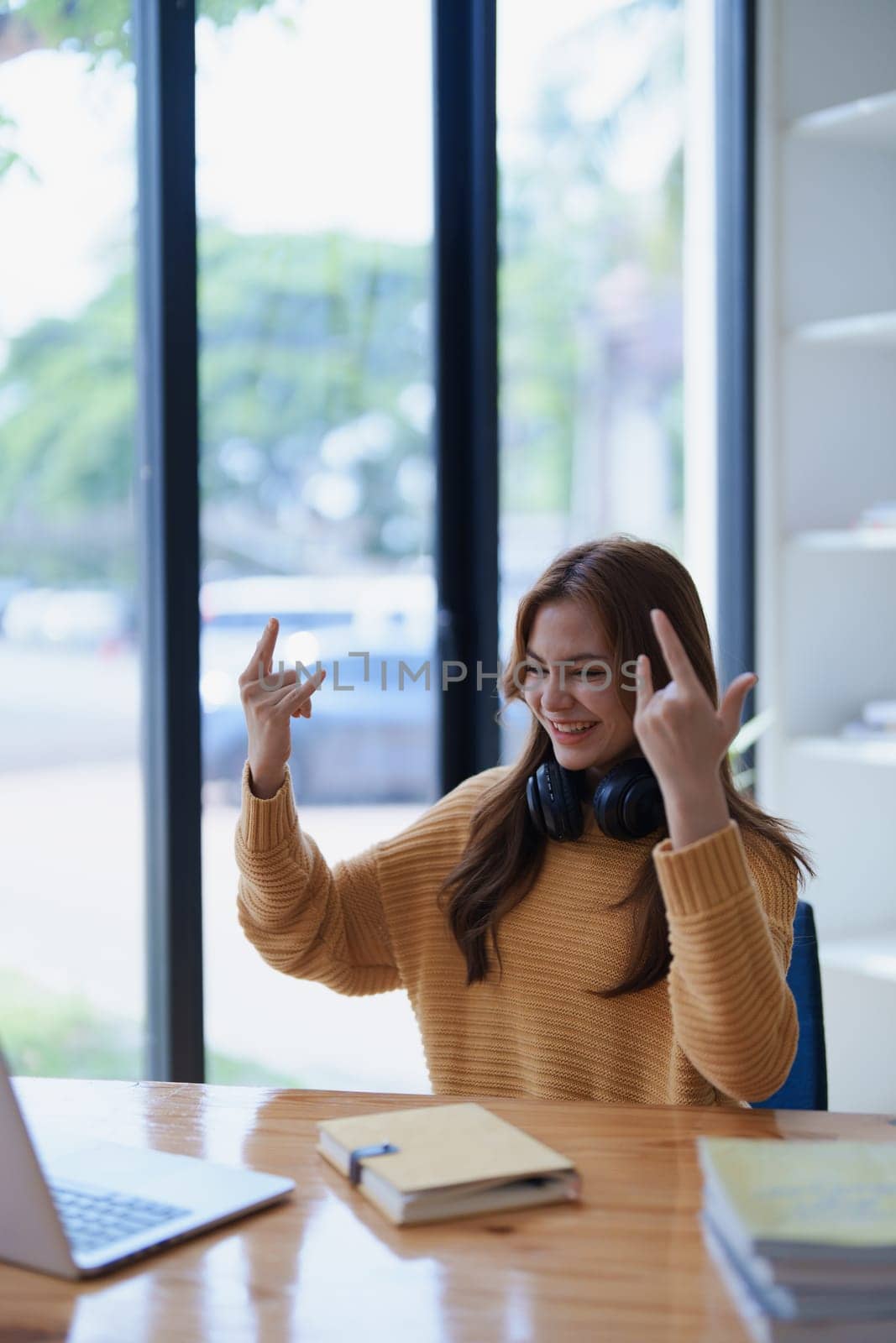Young woman cheerfully making rock and roll hand gestures at her desk..