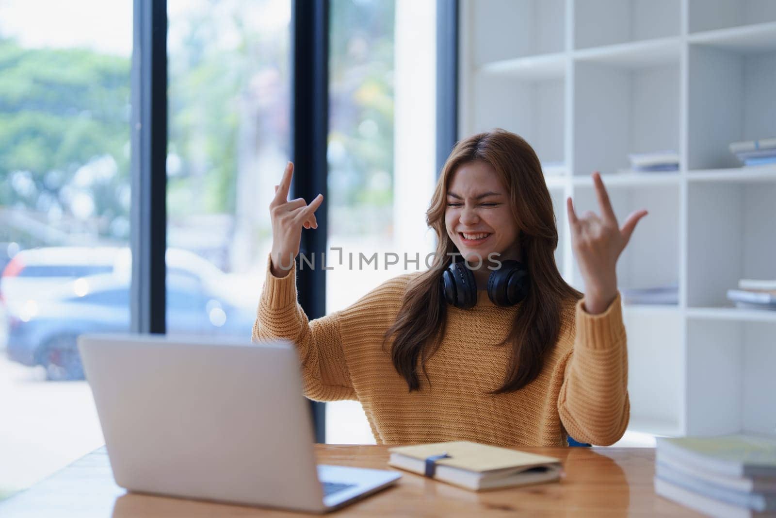 A young woman enthusiastically makes rock on hand gestures at her laptop..
