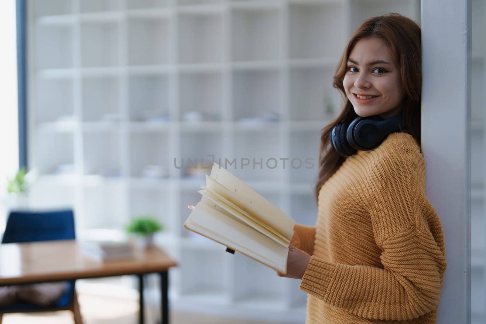 A young woman smiles while holding an open book in a bright modern office..