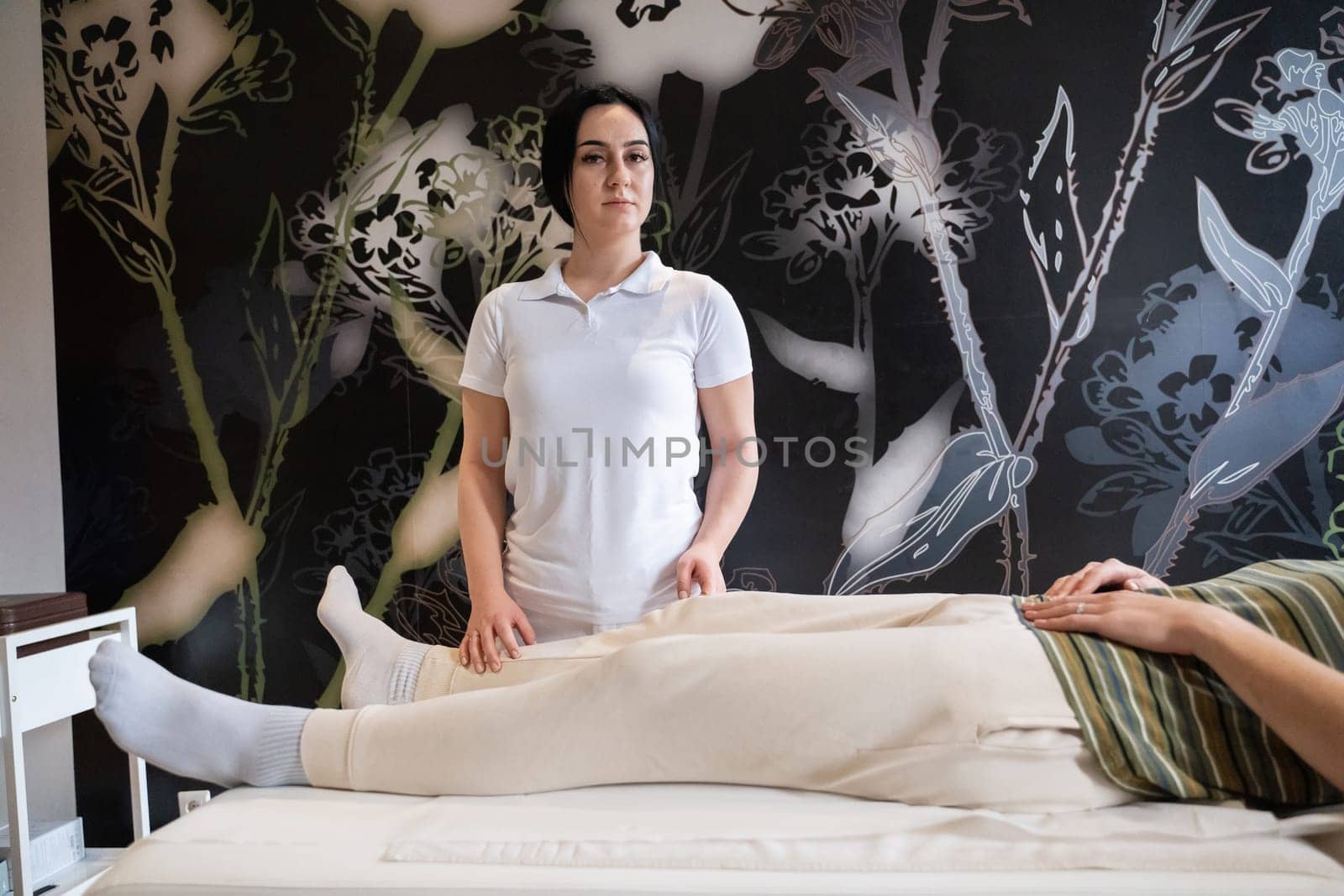 A therapist guiding a patient through leg exercises with the help of a blue foam roller in a therapy clinic.