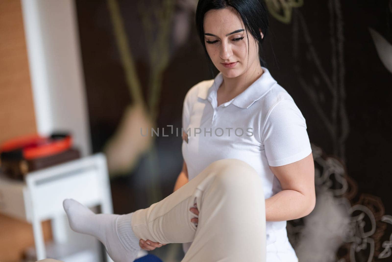 A therapist guiding a patient through leg exercises with the help of a blue foam roller in a therapy clinic.