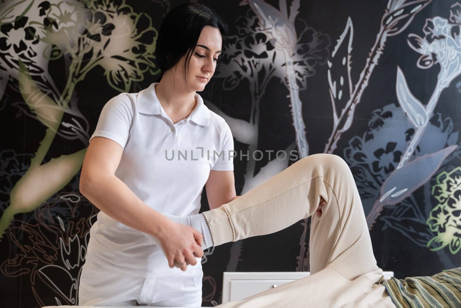 A therapist guiding a patient through leg exercises with the help of a blue foam roller in a therapy clinic.