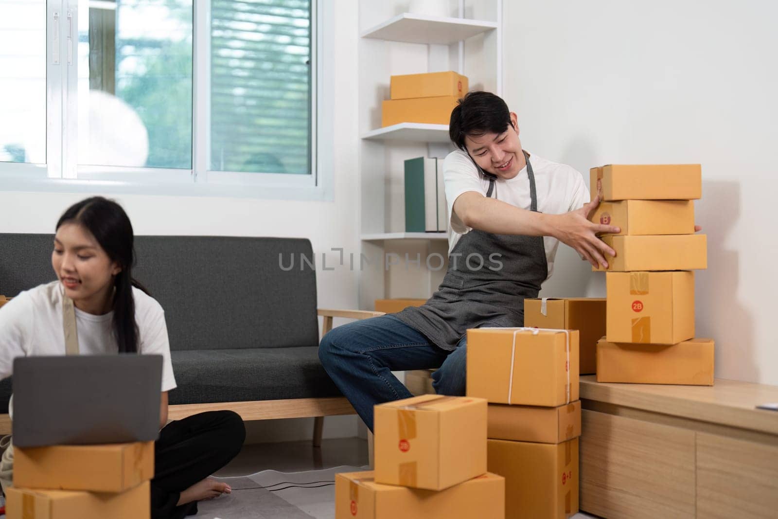 A playful couple in their home office, with one partner humorously struggling to balance stacked boxes, showcasing fun and teamwork.