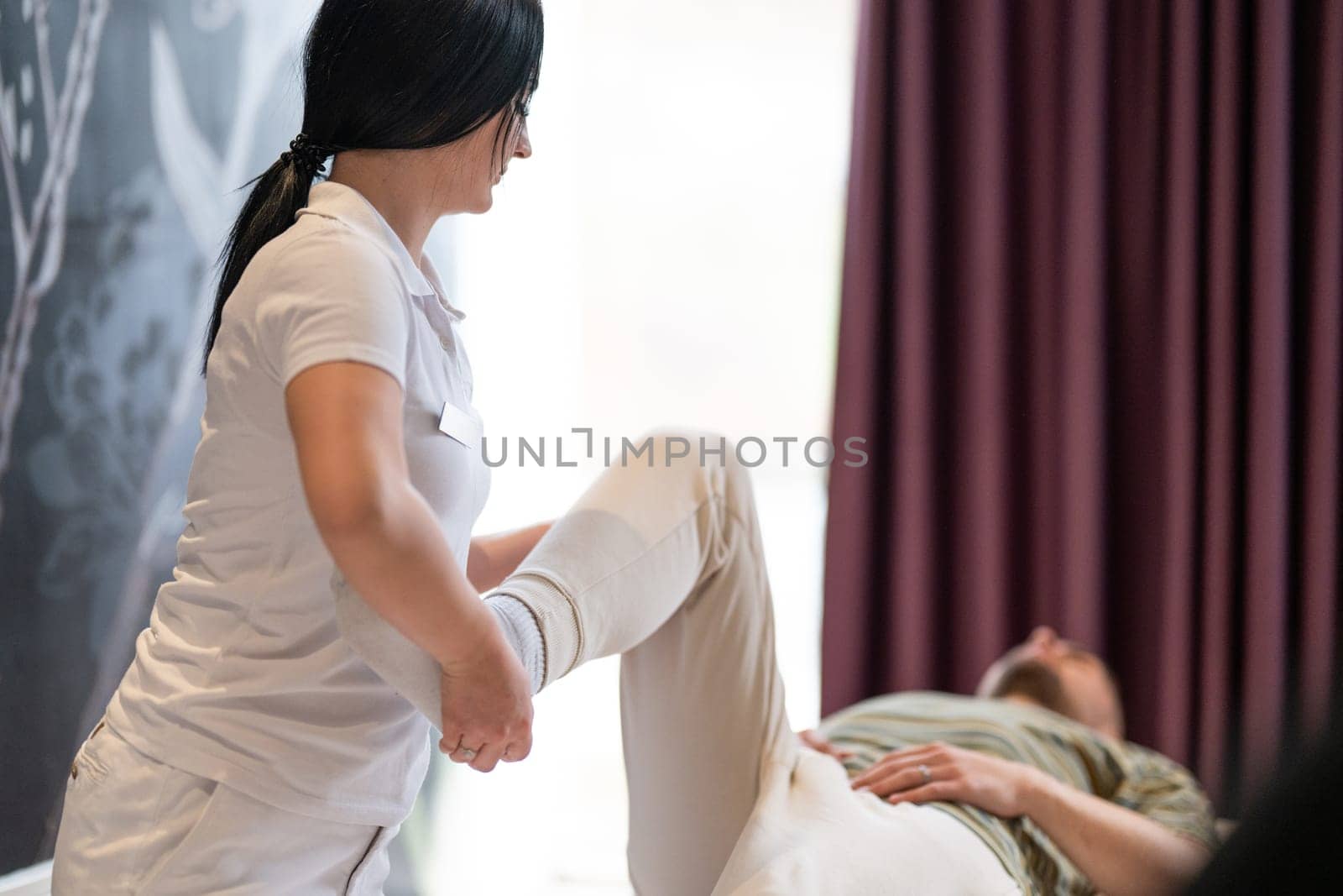 A therapist guiding a patient through leg exercises with the help of a blue foam roller in a therapy clinic.
