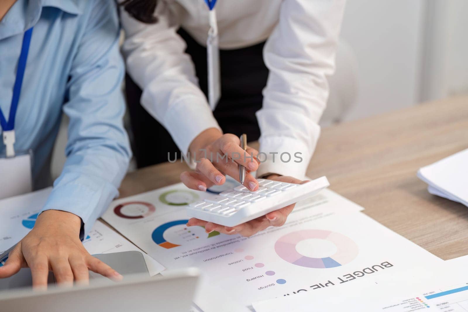 Women engaged in financial planning, using a calculator and documents to analyze budget data in a modern workspace.