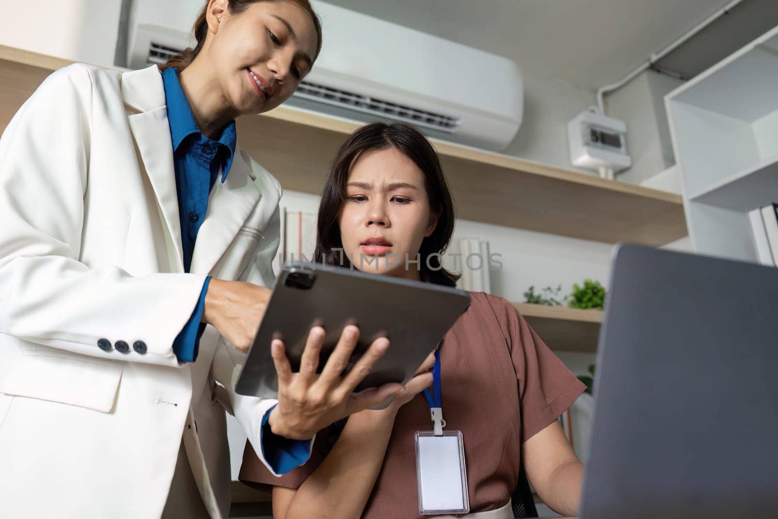 Two businesswomen examine digital tools on a tablet, reflecting the integration of technology in a contemporary office setting.