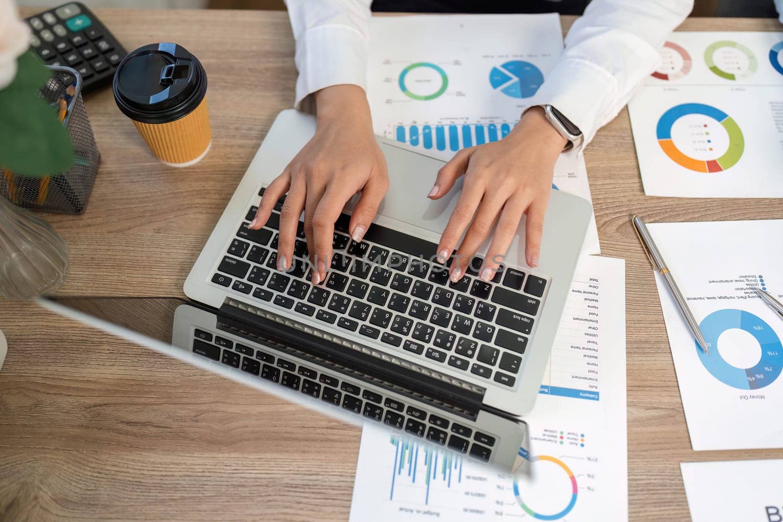 A business professional engaged in remote work, analyzing financial graphs and reports on a laptop, showcasing productivity and focus.