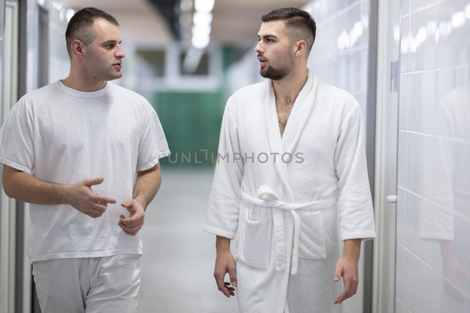 Medical Consultation in Spa Corridor.Two men discussing treatment options while walking through a clinical spa corridor, wearing white uniforms and bathrobe