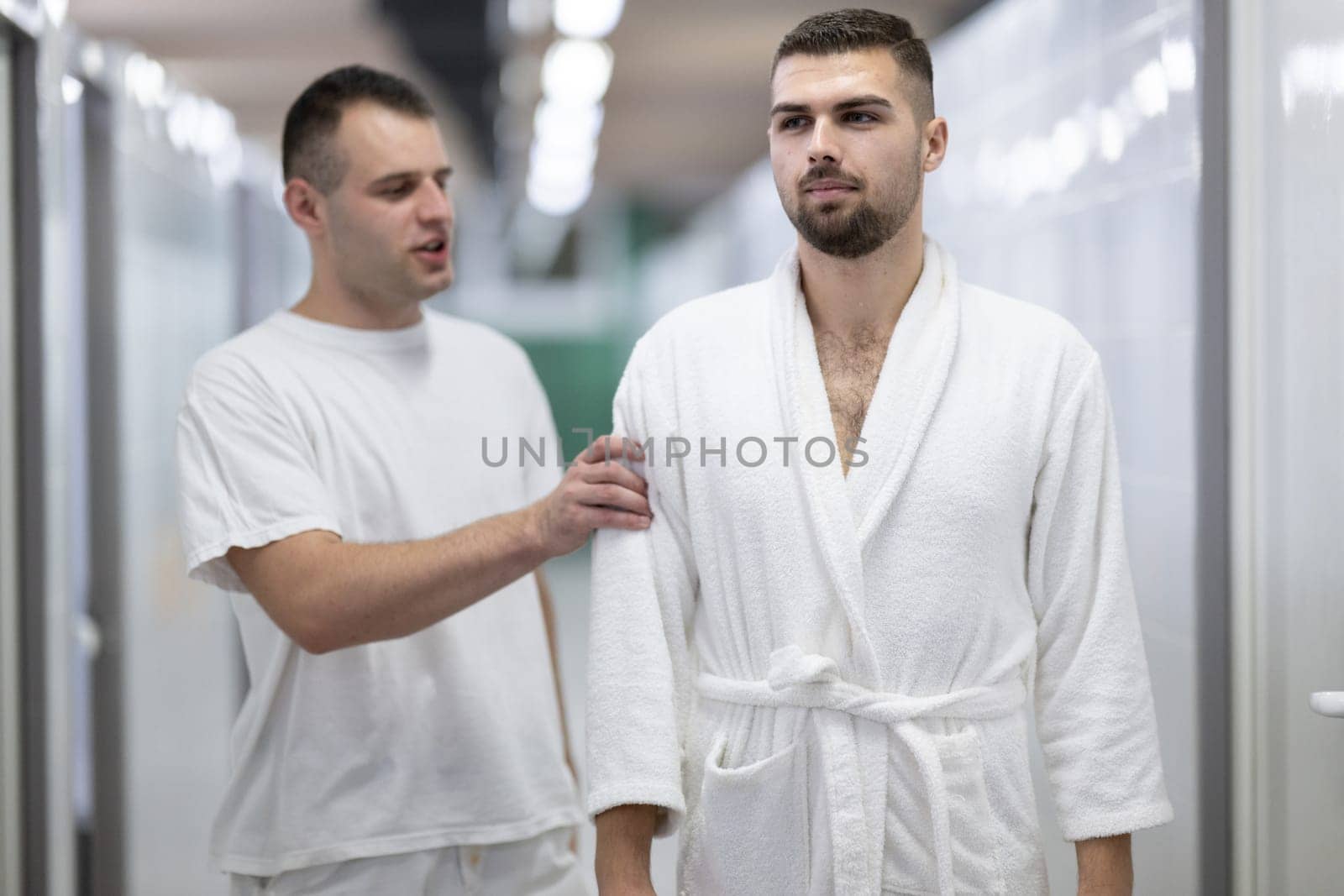 Medical Consultation in Spa Corridor.Two men discussing treatment options while walking through a clinical spa corridor, wearing white uniforms and bathrobe