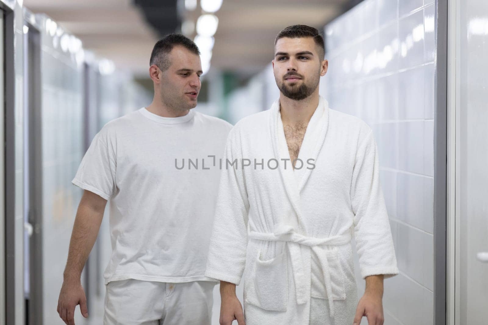 Medical Consultation in Spa Corridor.Two men discussing treatment options while walking through a clinical spa corridor, wearing white uniforms and bathrobe