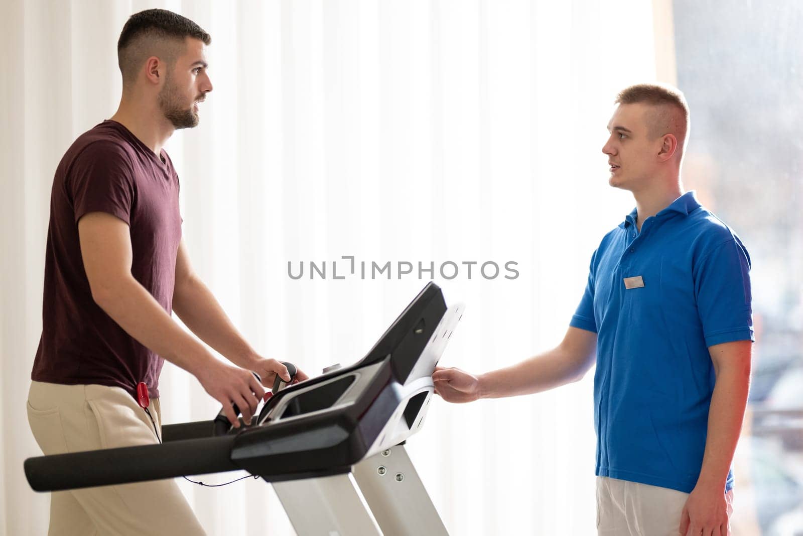 Man undergoing physical therapy with trainer assistance on a treadmill indoors.