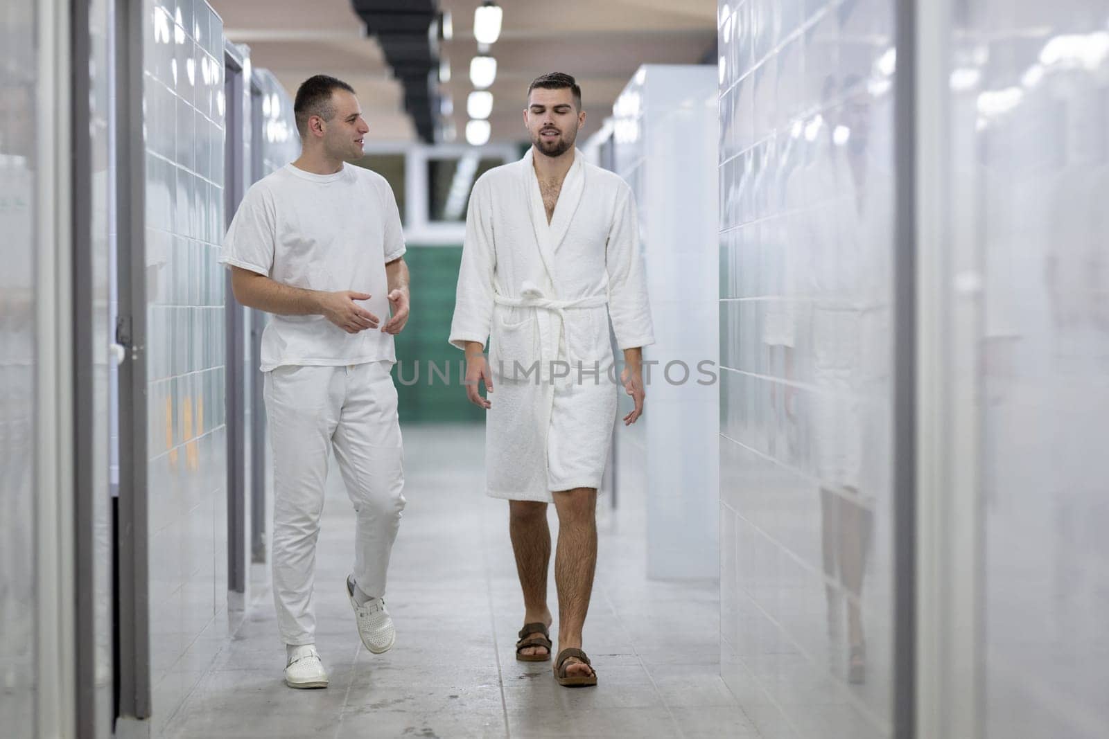 Medical Consultation in Spa Corridor.Two men discussing treatment options while walking through a clinical spa corridor, wearing white uniforms and bathrobe