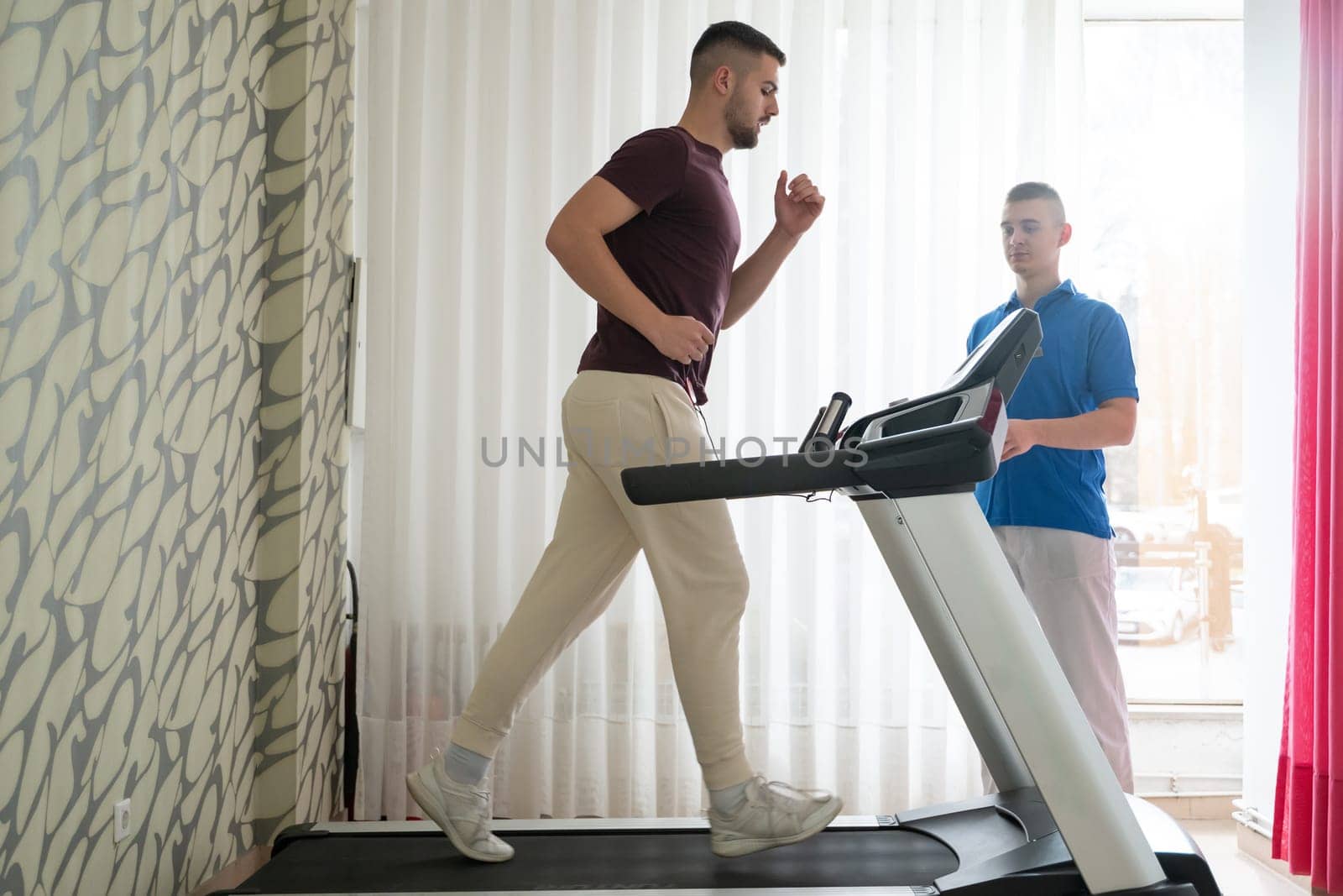 Man undergoing physical therapy with trainer assistance on a treadmill indoors.