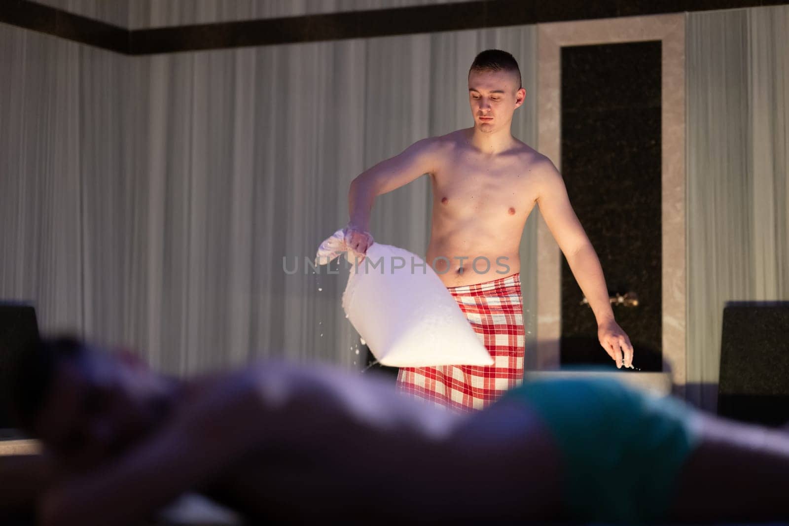 Hamam Attendant with Towel.Young male attendant preparing towel in traditional Turkish bath, standing near client